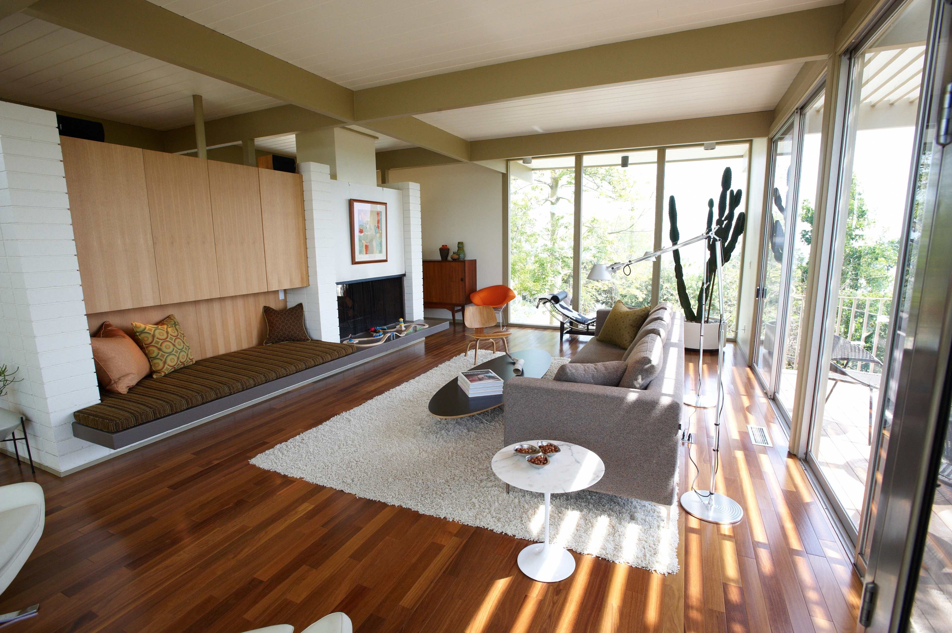 A modern living room featuring a sofa, a small round table, a floor lamp, and large windows with natural light, along with a wooden floor and a minimalist design.