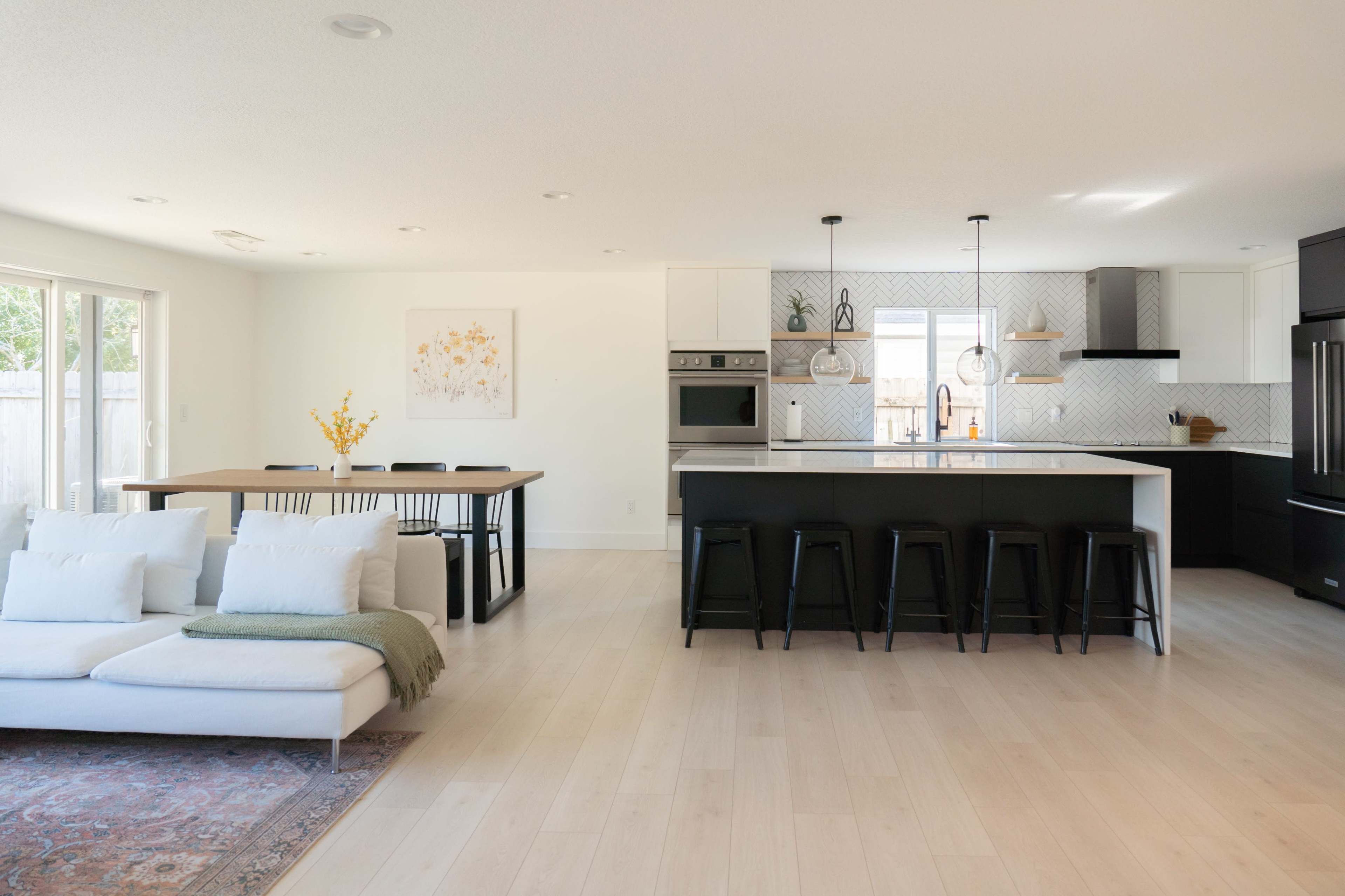 A modern kitchen and dining area featuring a large island, bar seating, a dining table, and sliding glass doors that lead to an outdoor space.