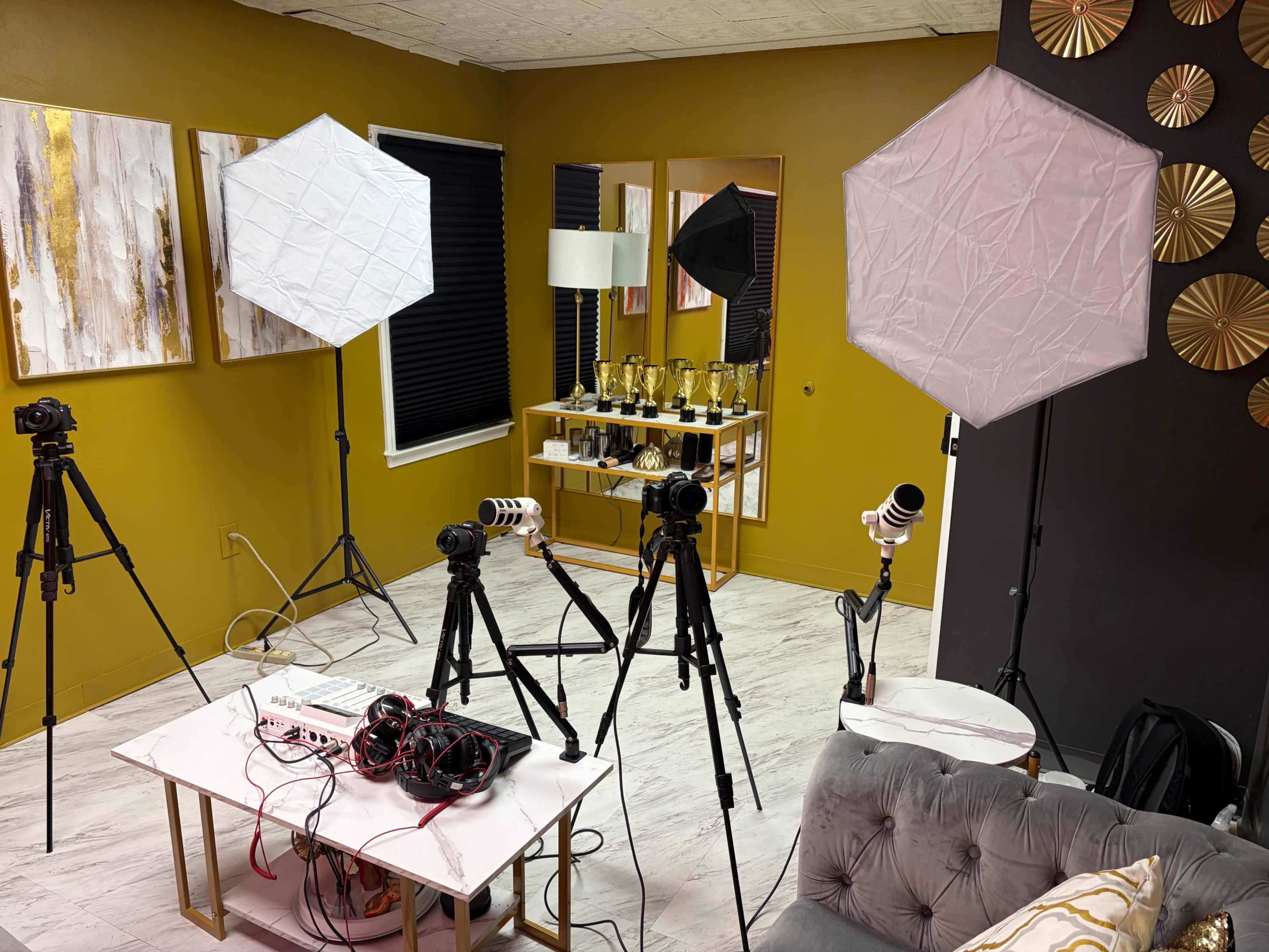The image shows a well-lit studio space equipped with multiple tripods, softbox lights, and a table with recording equipment.
