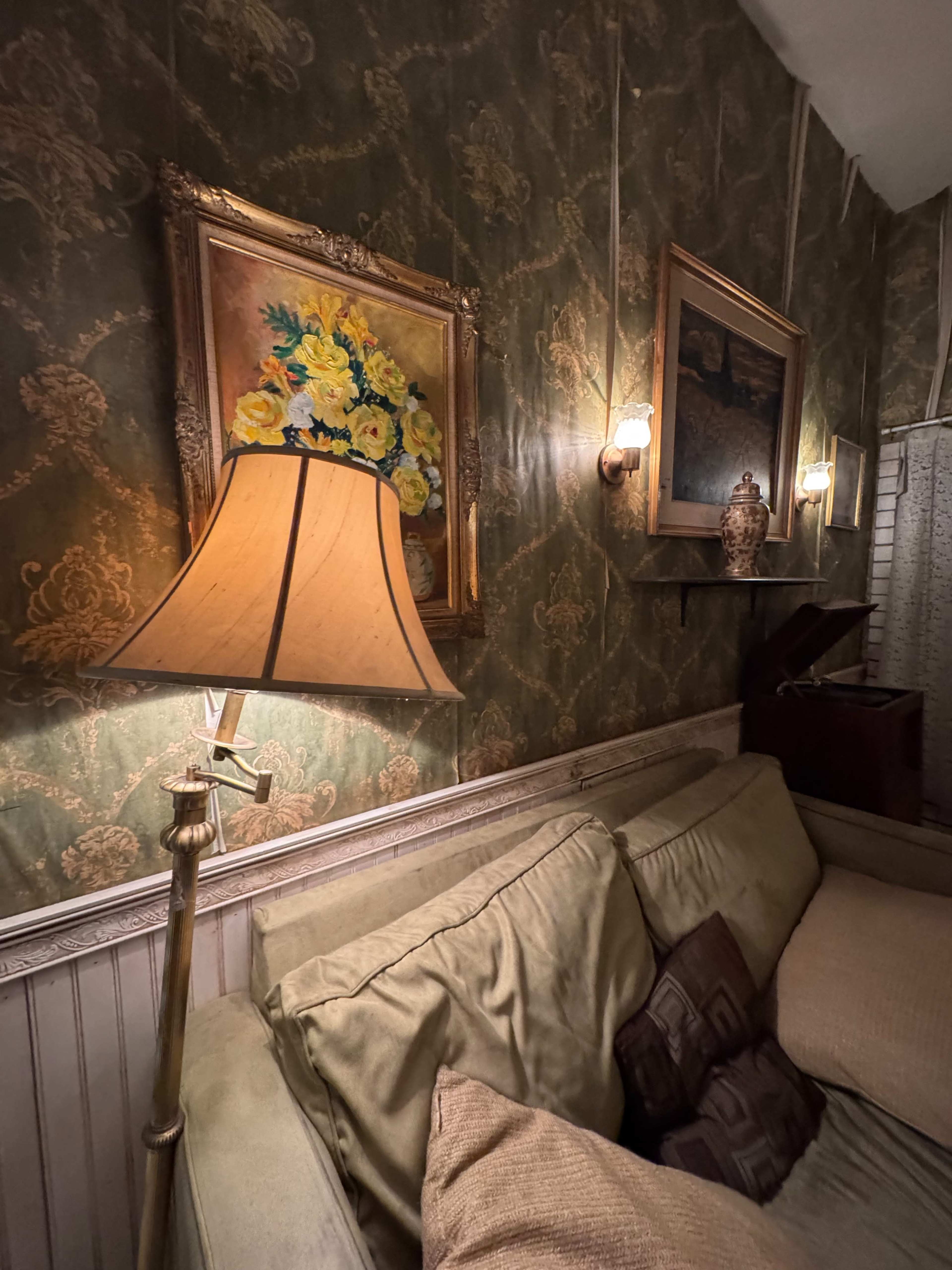 The image shows a cozy living room corner featuring a couch, framed paintings on the wall, and a lamp illuminating the space.
