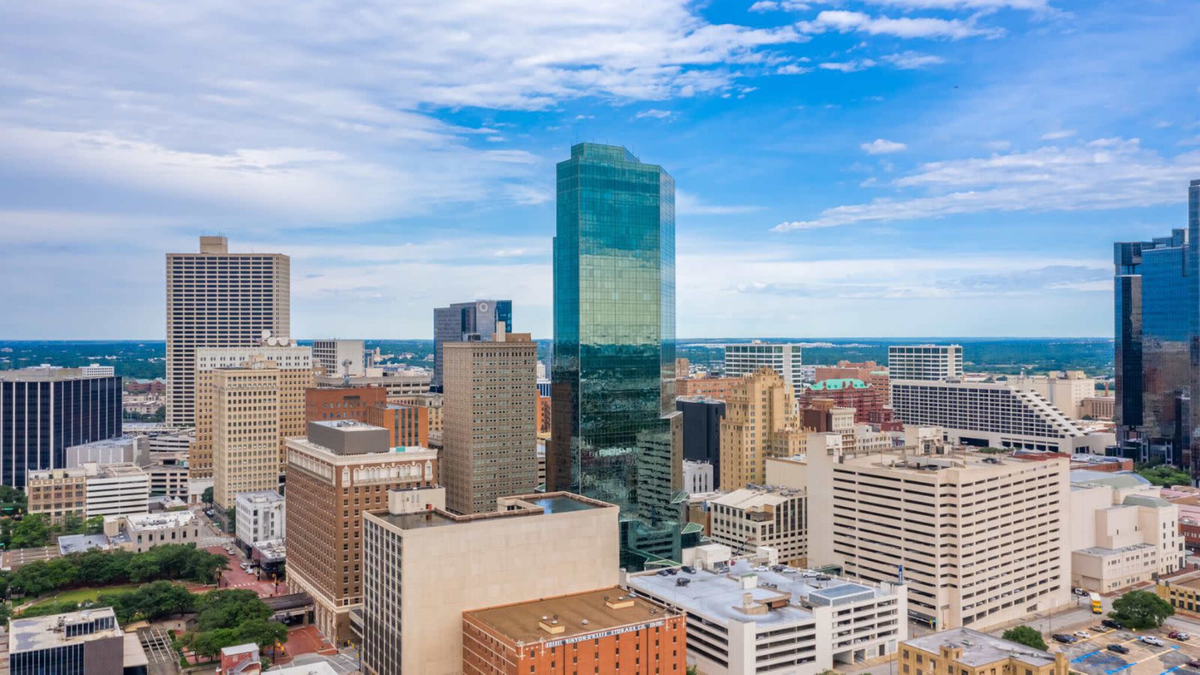 An aerial view of a city skyline featuring modern skyscrapers and a mix of architectural styles under a partly cloudy sky.