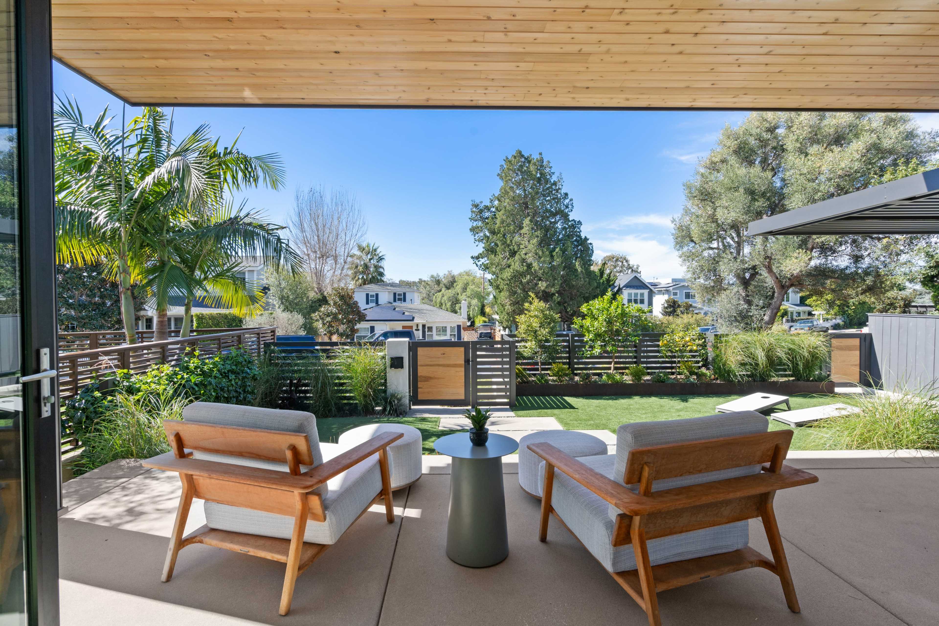 A patio area with two wooden chairs facing a landscaped backyard and modern house design.