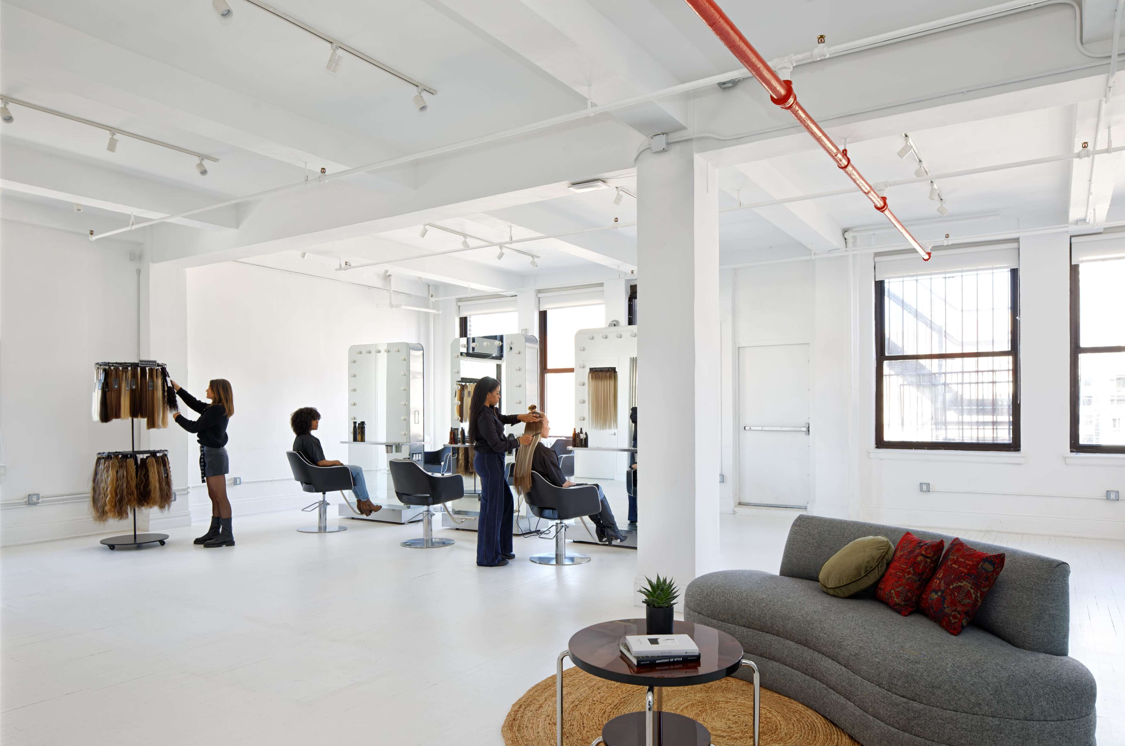 A modern hair salon with multiple styling stations and some clients receiving hair services.