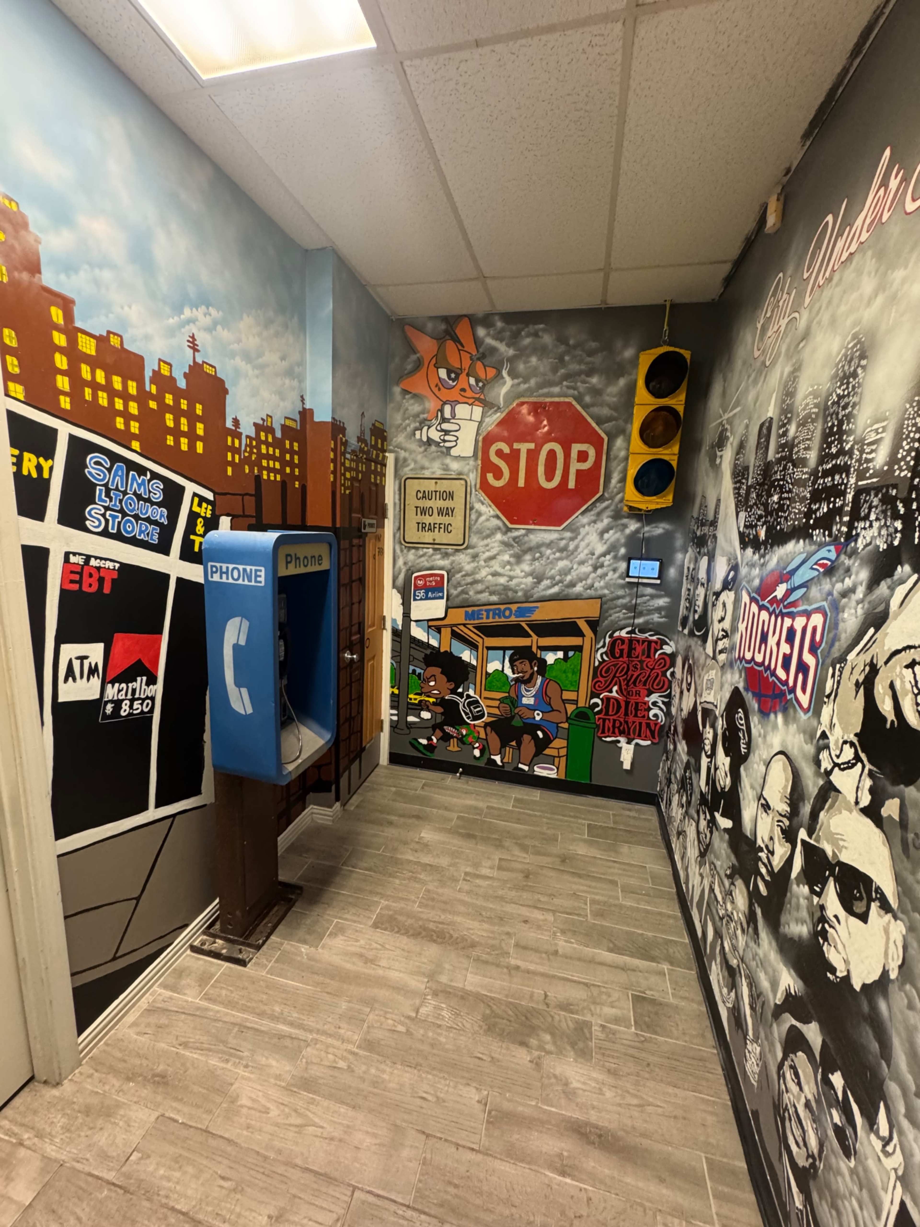 The image shows a vibrant hallway decorated with street art, featuring a payphone, a traffic light, and various murals depicting urban scenes and characters.