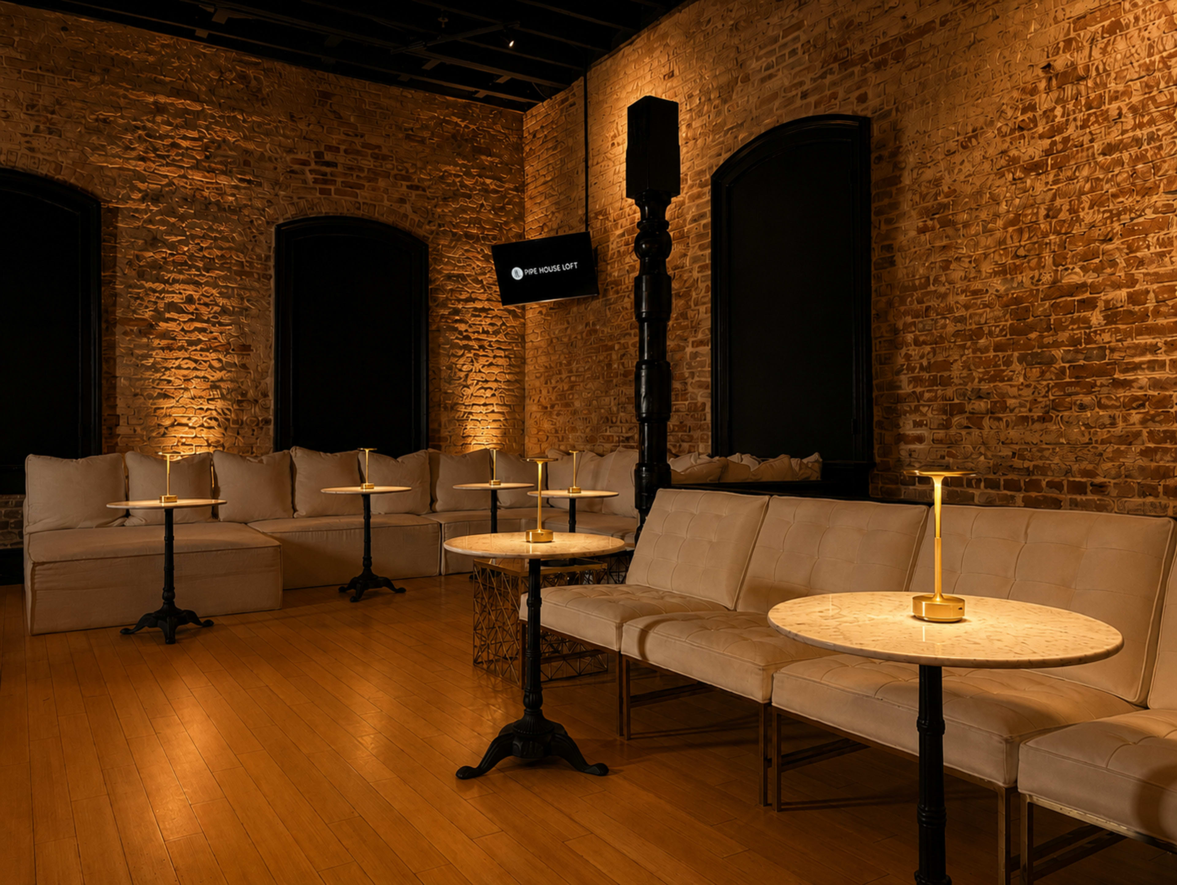 A modern lounge features exposed brick walls, plush seating, and elegant tables with soft lighting.