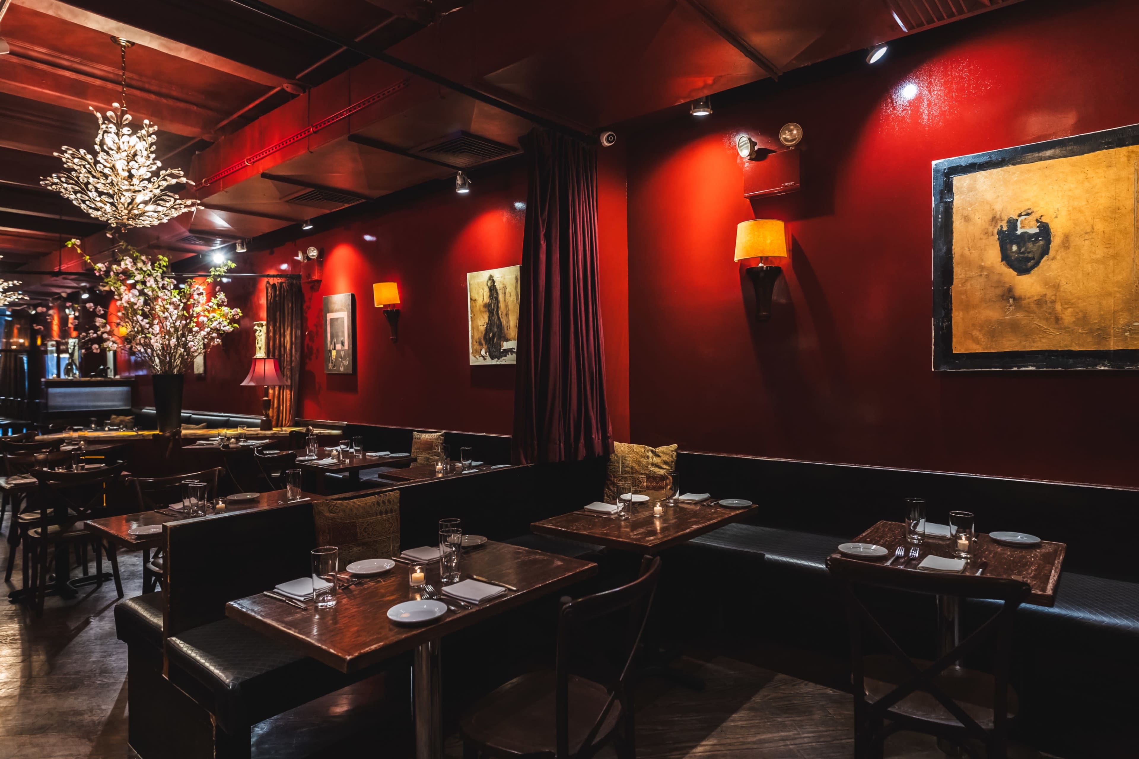 The image shows a dimly lit restaurant with red walls, wooden tables, and artwork hanging on the walls.
