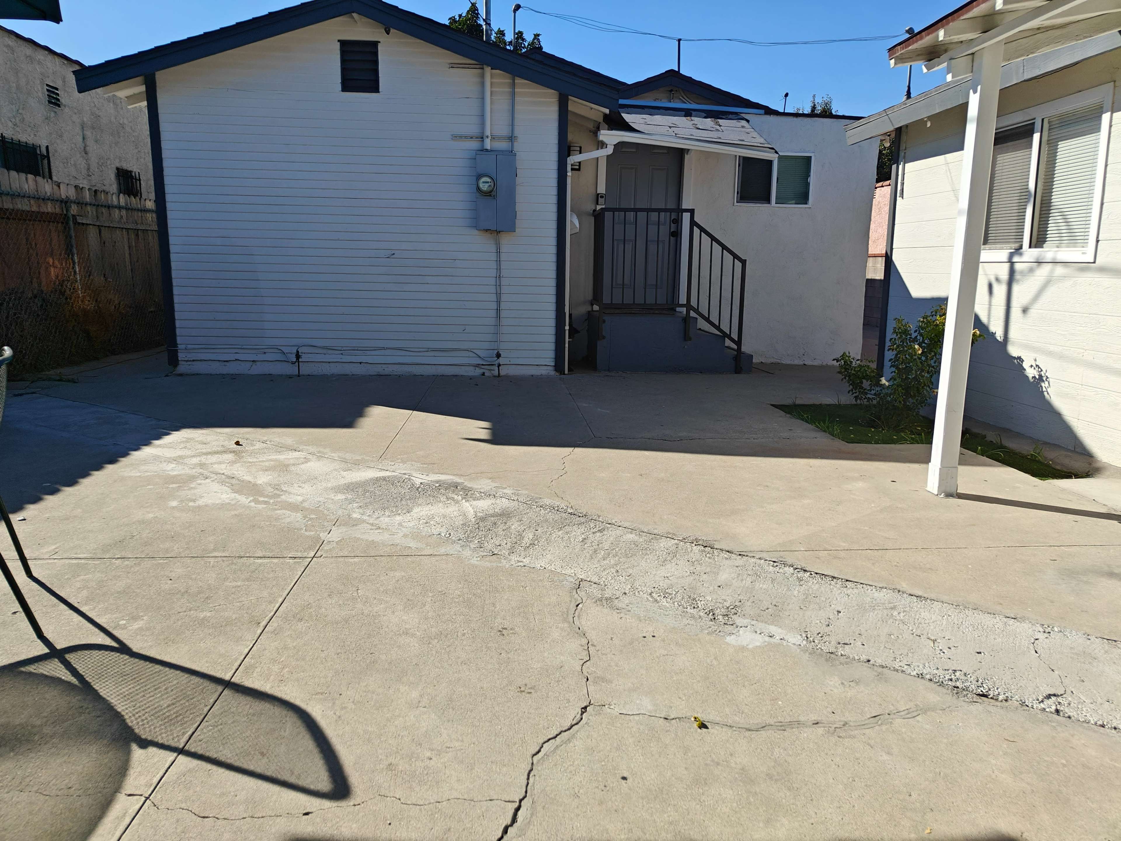 The image shows a concrete patio area leading to a white building with a blue roof and a staircase.