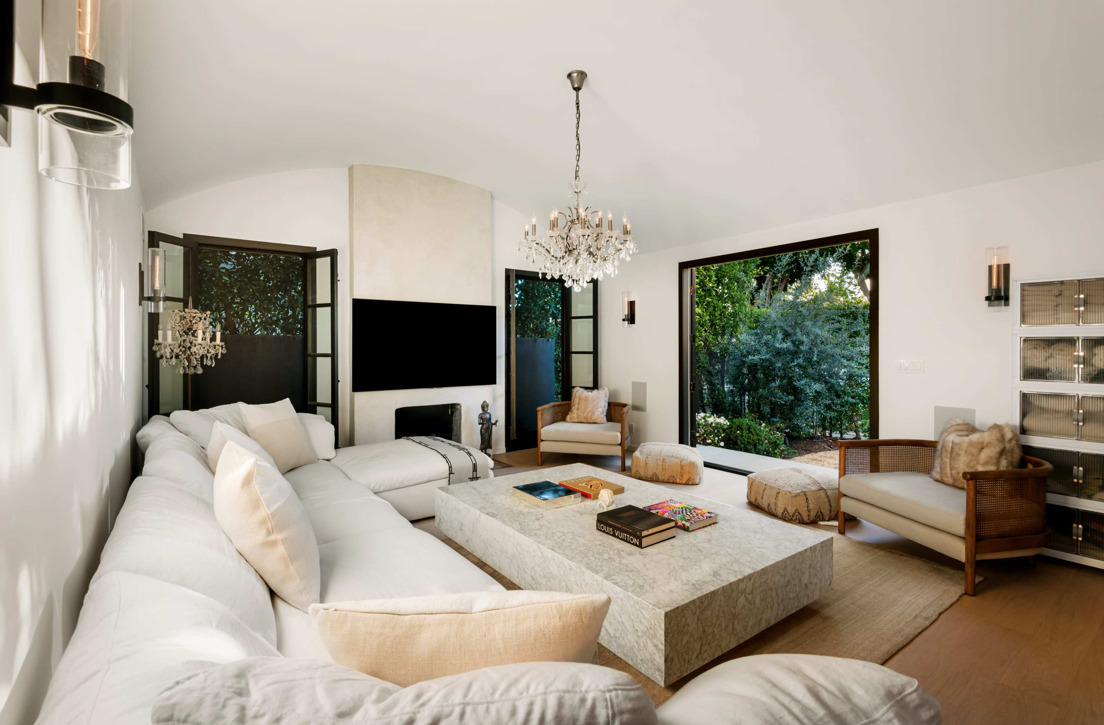 The living room features a spacious sectional sofa, a large stone coffee table, and two armchairs, with large windows overlooking a garden.