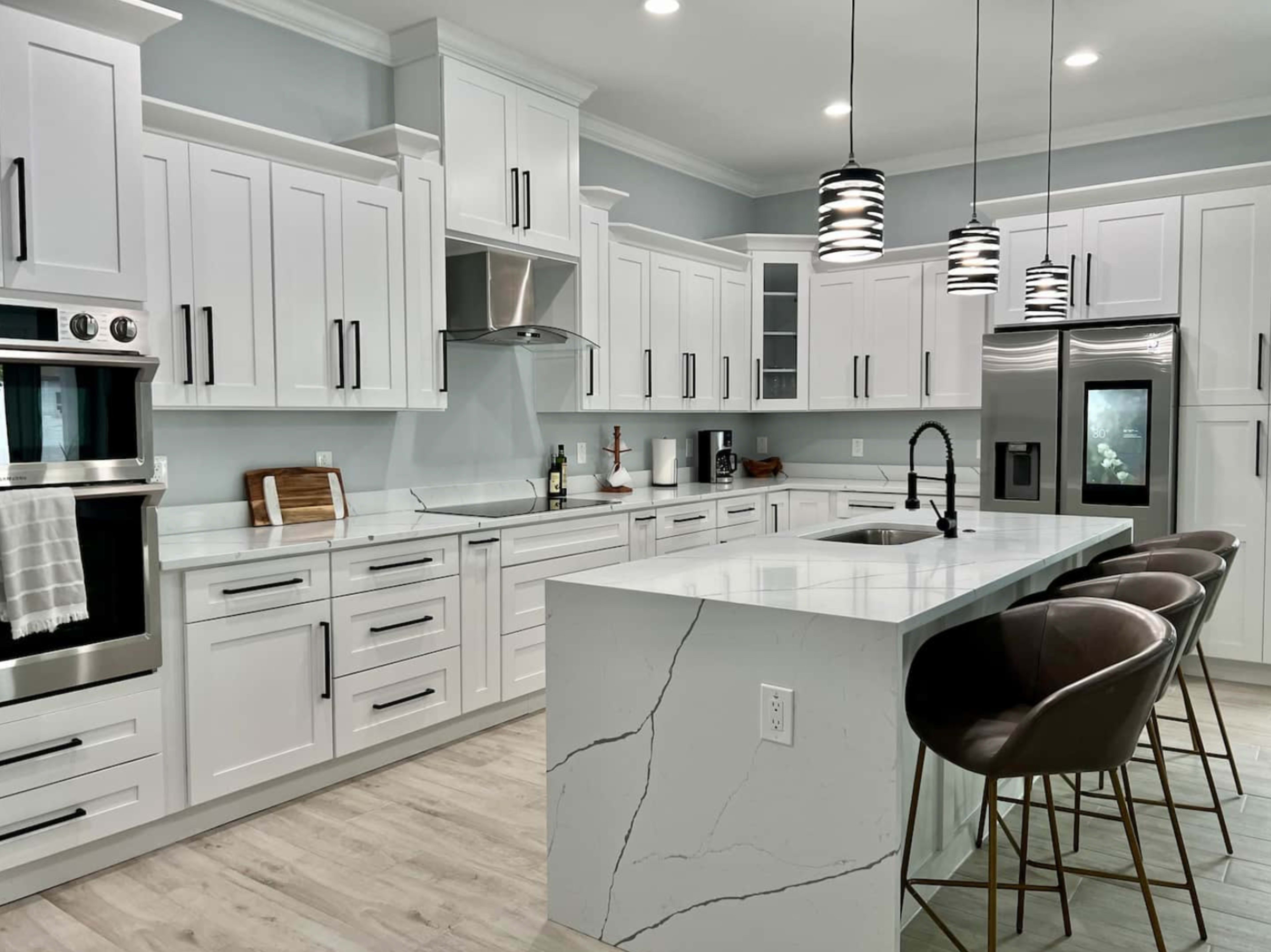 A modern kitchen features white cabinetry, stainless steel appliances, a marble-topped island, and multiple pendant lights.