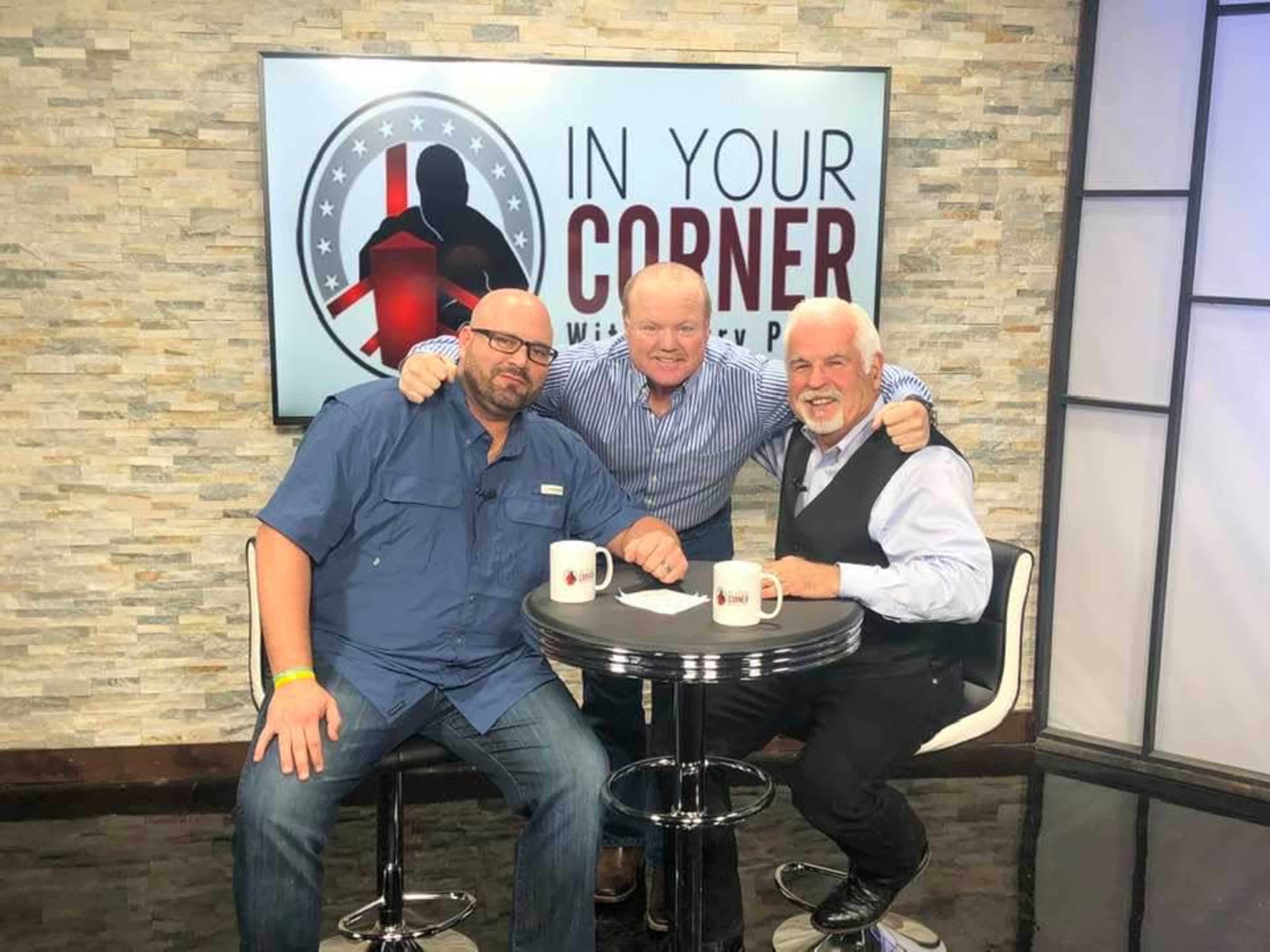 Three men sit together around a table on a television set with the backdrop reading "In Your Corner with Pat."
