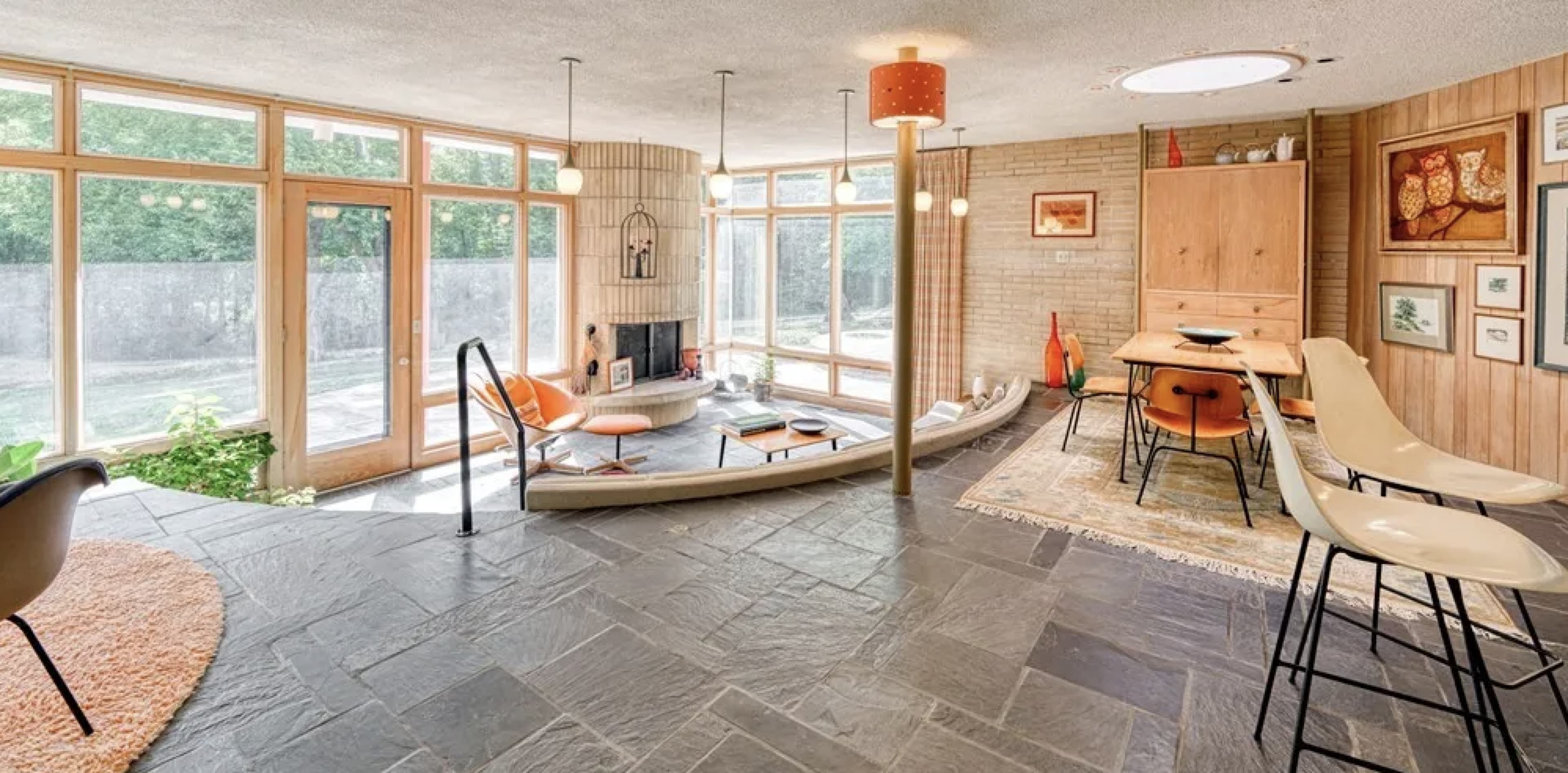 The image depicts a modern, sunlit indoor space with large windows, a stone floor, and distinct areas for seating and dining.