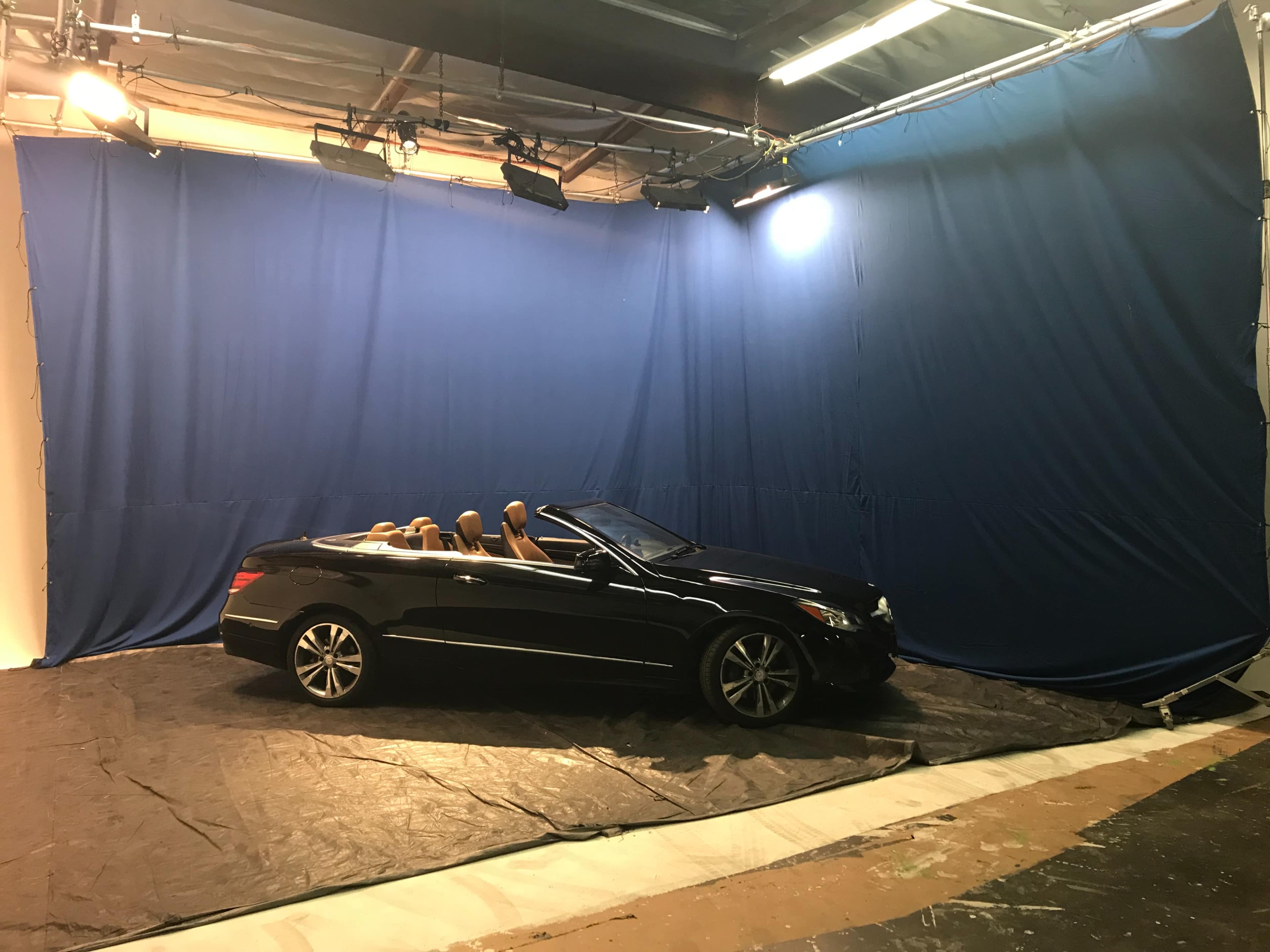 A black convertible car is parked in a studio with a blue backdrop and studio lighting.