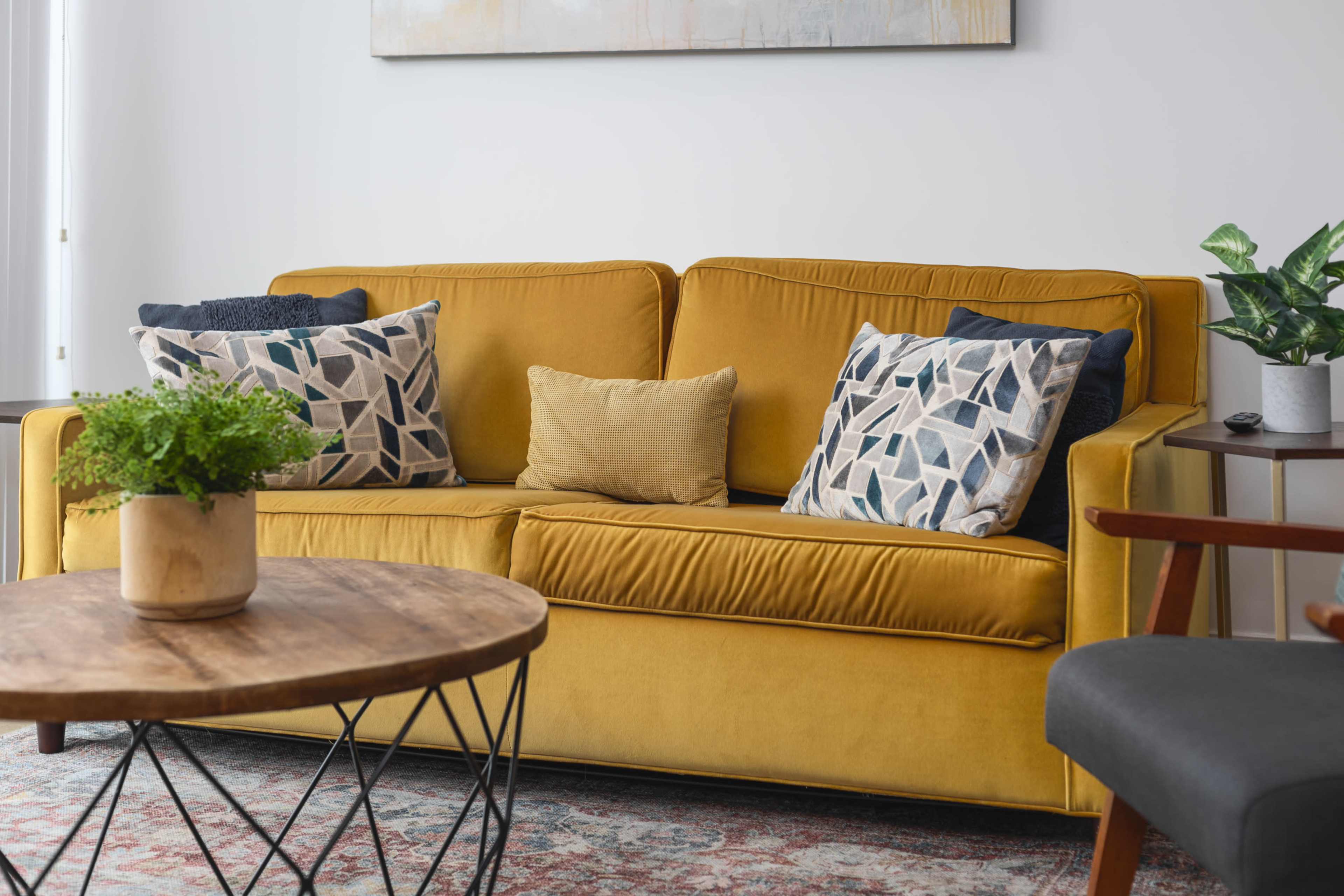 The image shows a yellow couch with patterned cushions and a wooden coffee table in a modern living room setting.