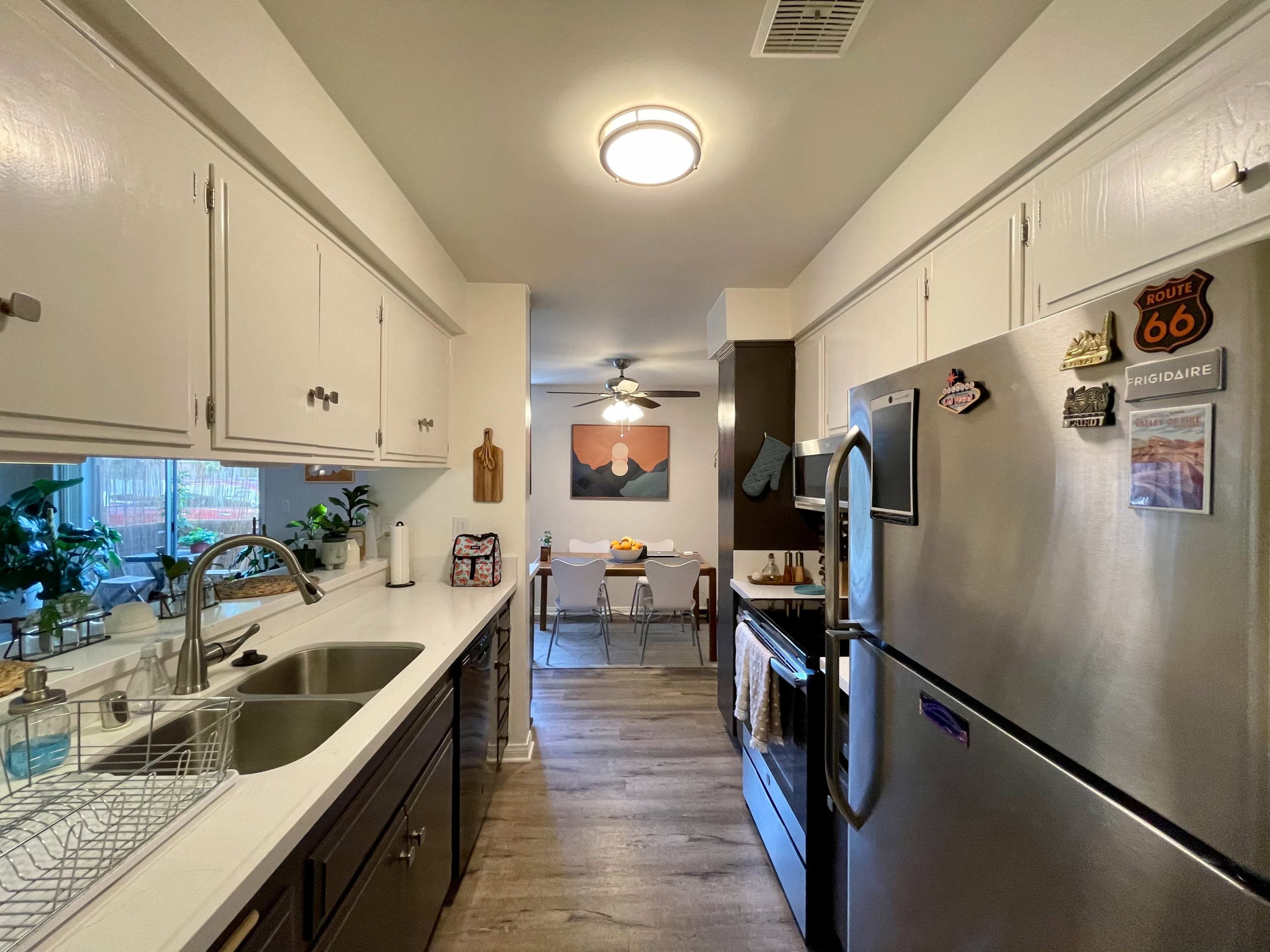 A kitchen with white cabinetry, stainless steel appliances, and a view into a dining area featuring a table with chairs and a wall art piece.