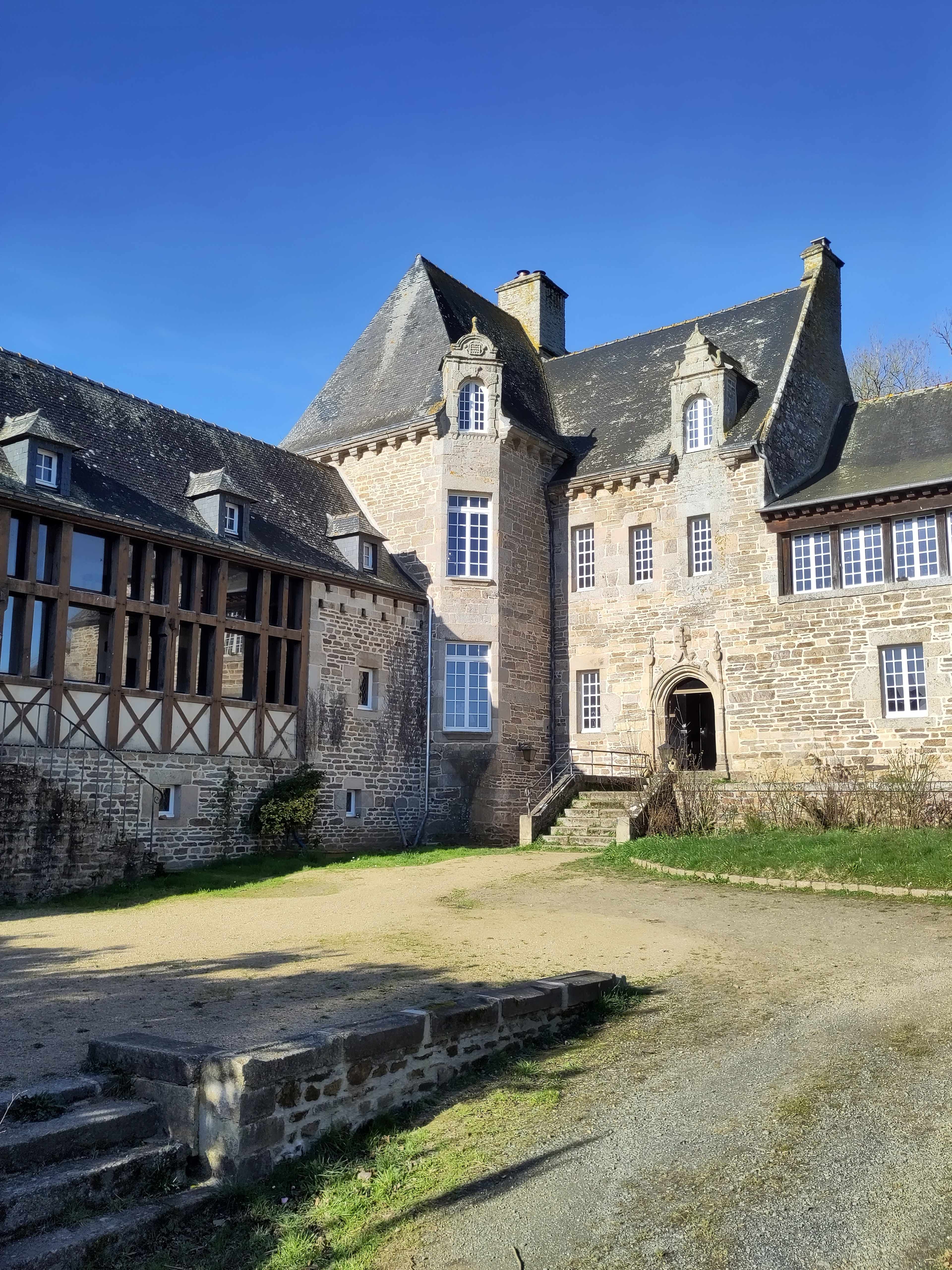 The image features a historic stone building with a pointed roof and large windows, surrounded by a grassy area and a clear blue sky.