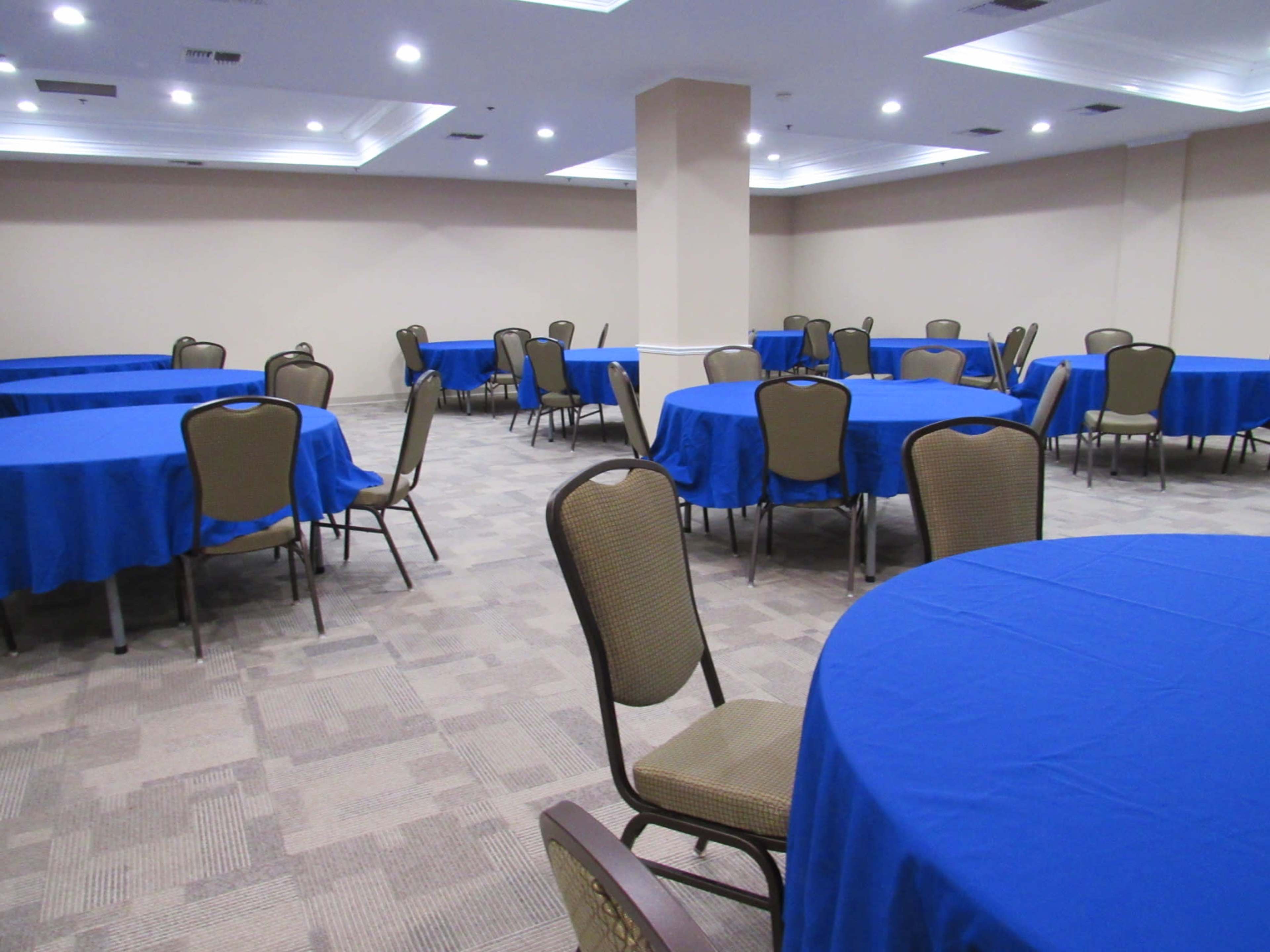 A banquet room filled with several round tables covered in blue tablecloths and surrounded by chairs.