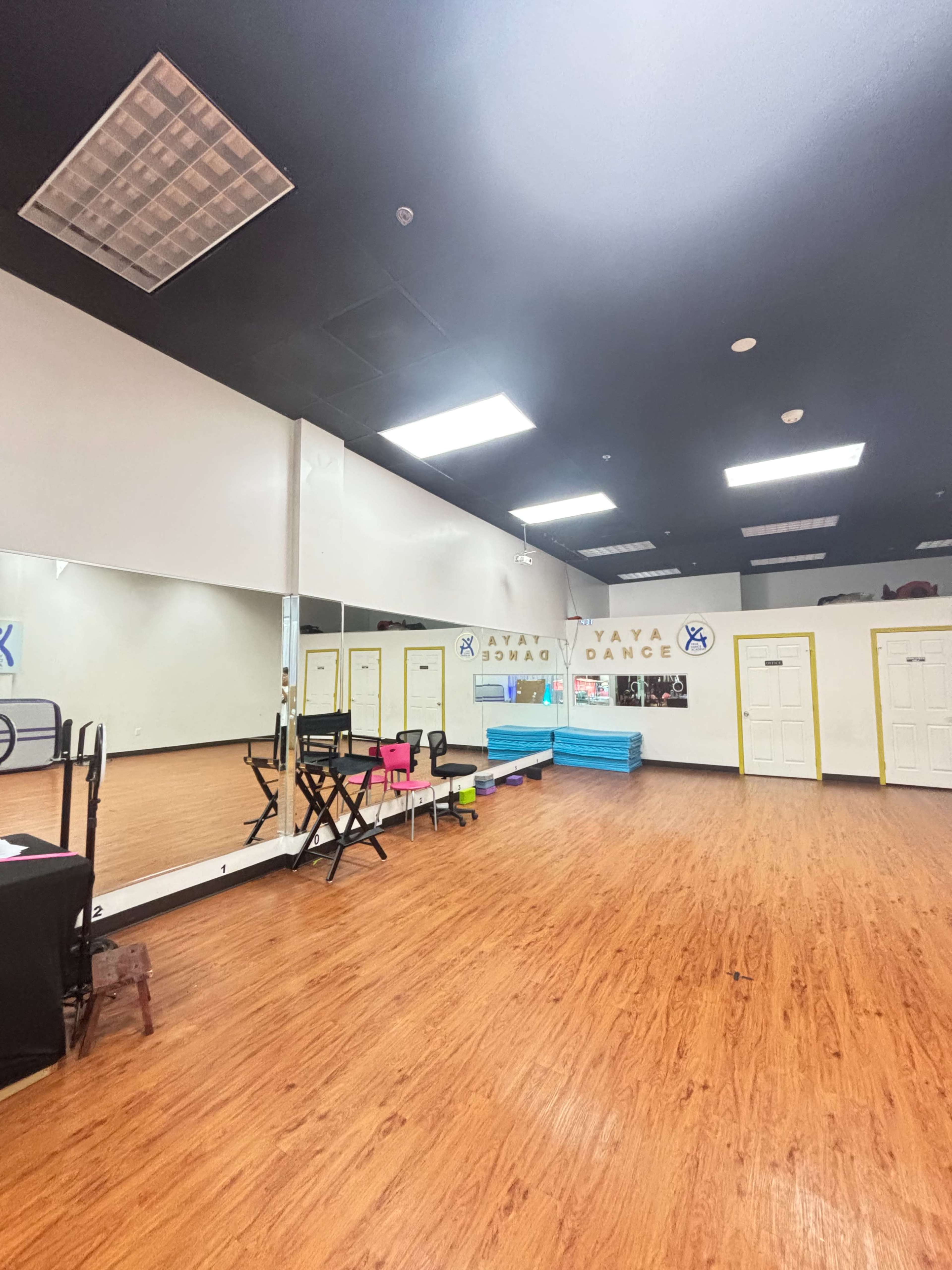 The image shows a spacious dance studio with mirrored walls, wooden flooring, and bright overhead lights.