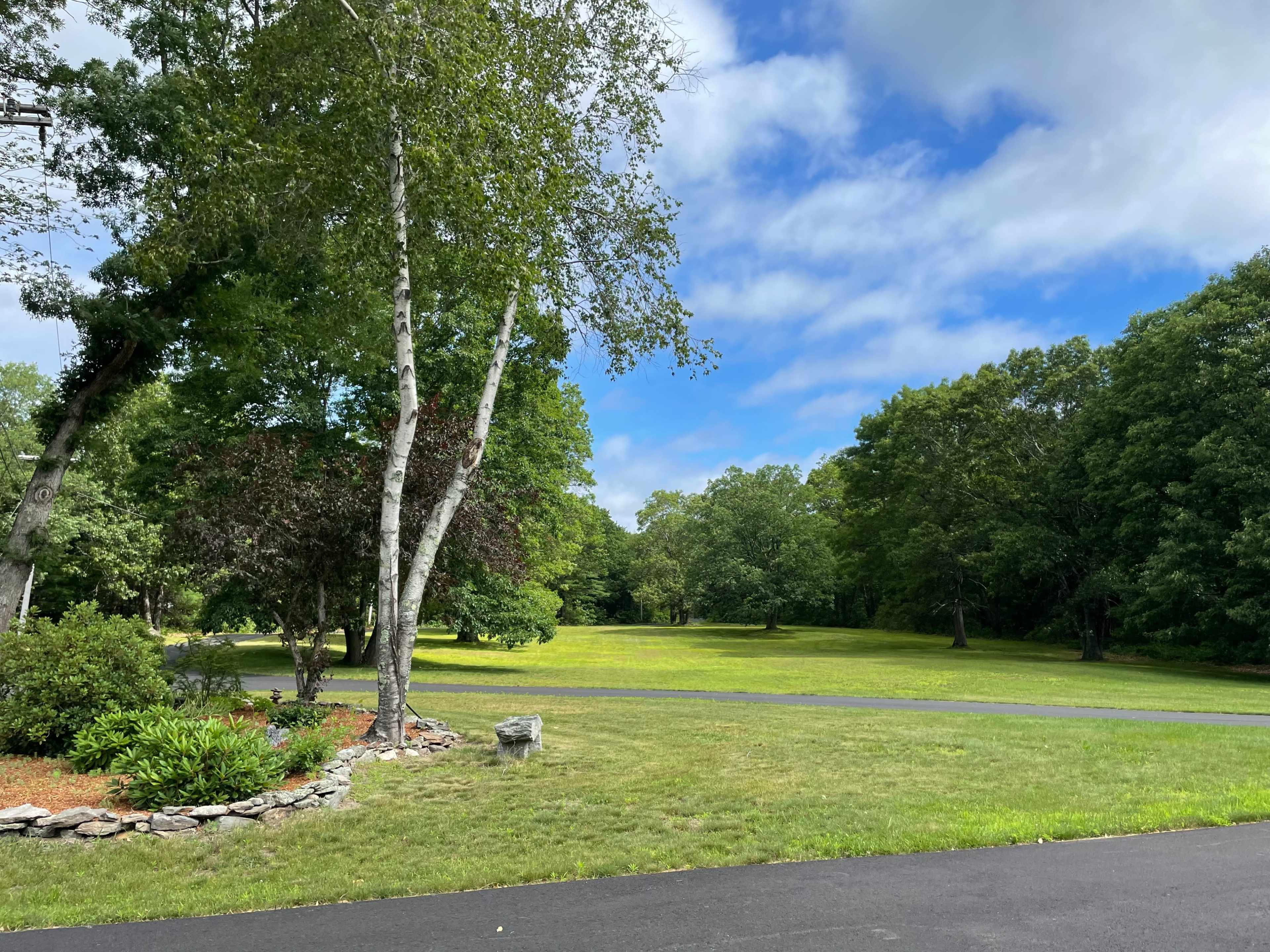 A spacious grassy area is surrounded by trees under a partly cloudy sky.