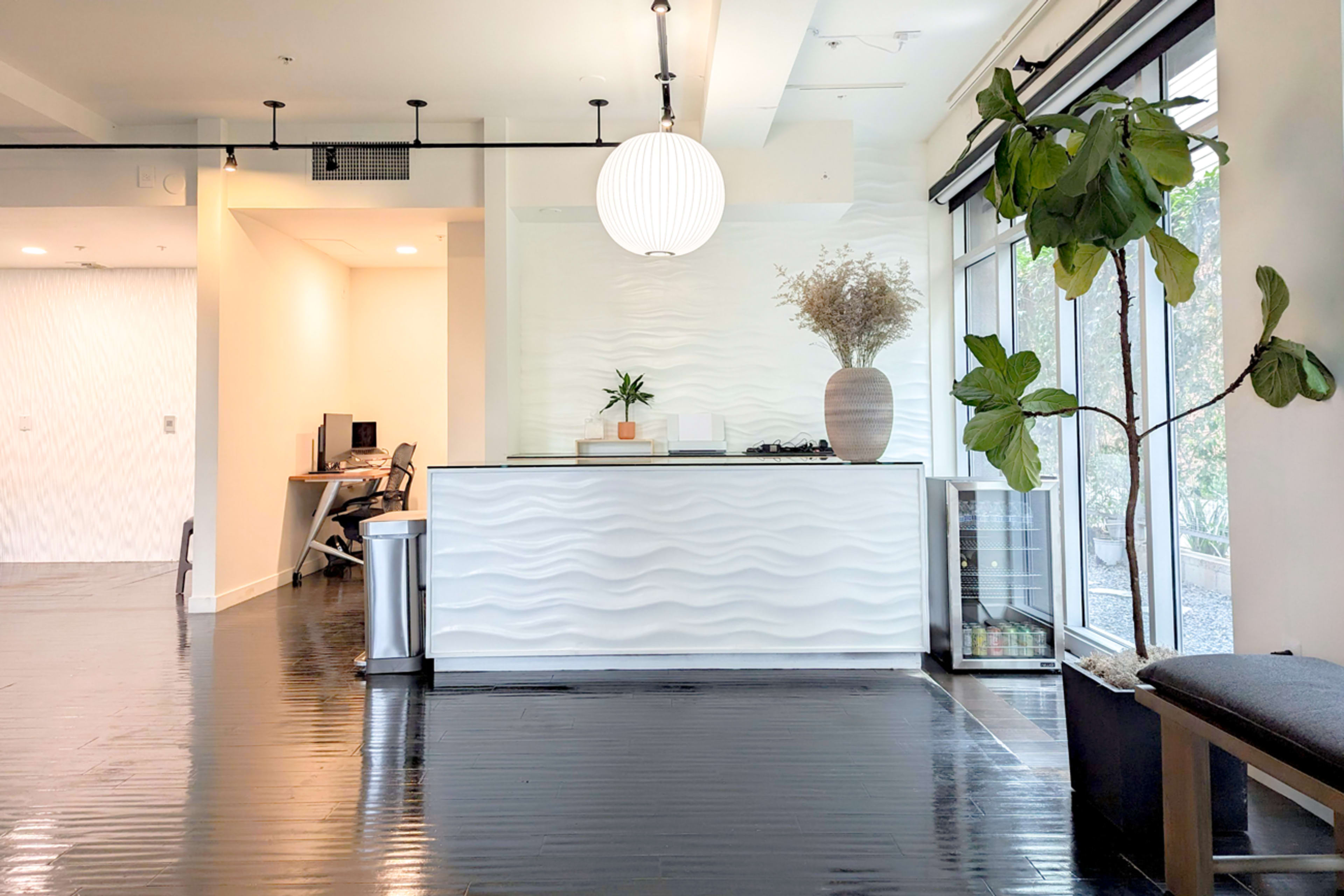 A modern reception area with a wavy white counter, a large round pendant light, and greenery in decorative pots.