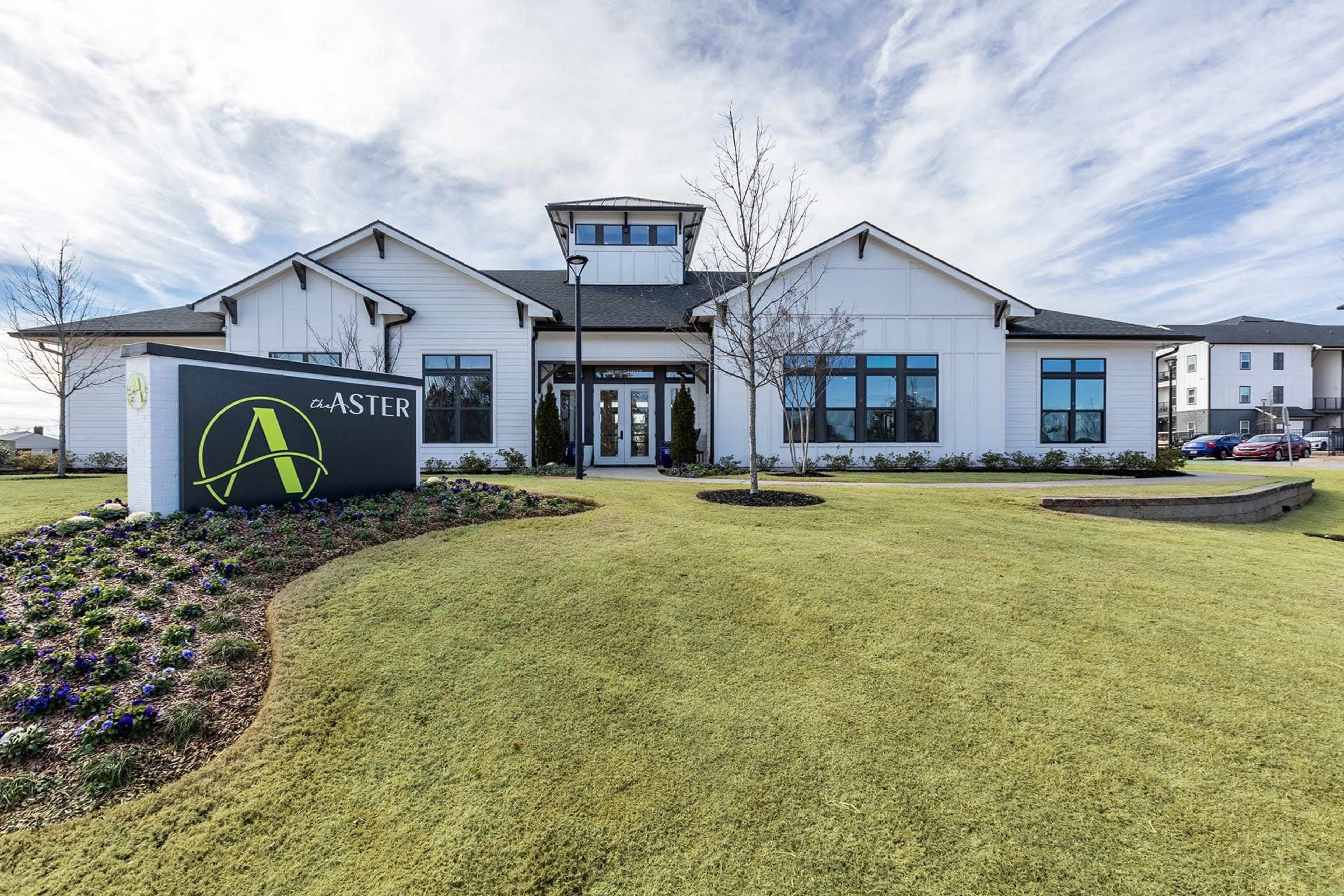 A modern building with a prominent sign reading "ASTERS" in a landscaped yard featuring green grass and flower beds.