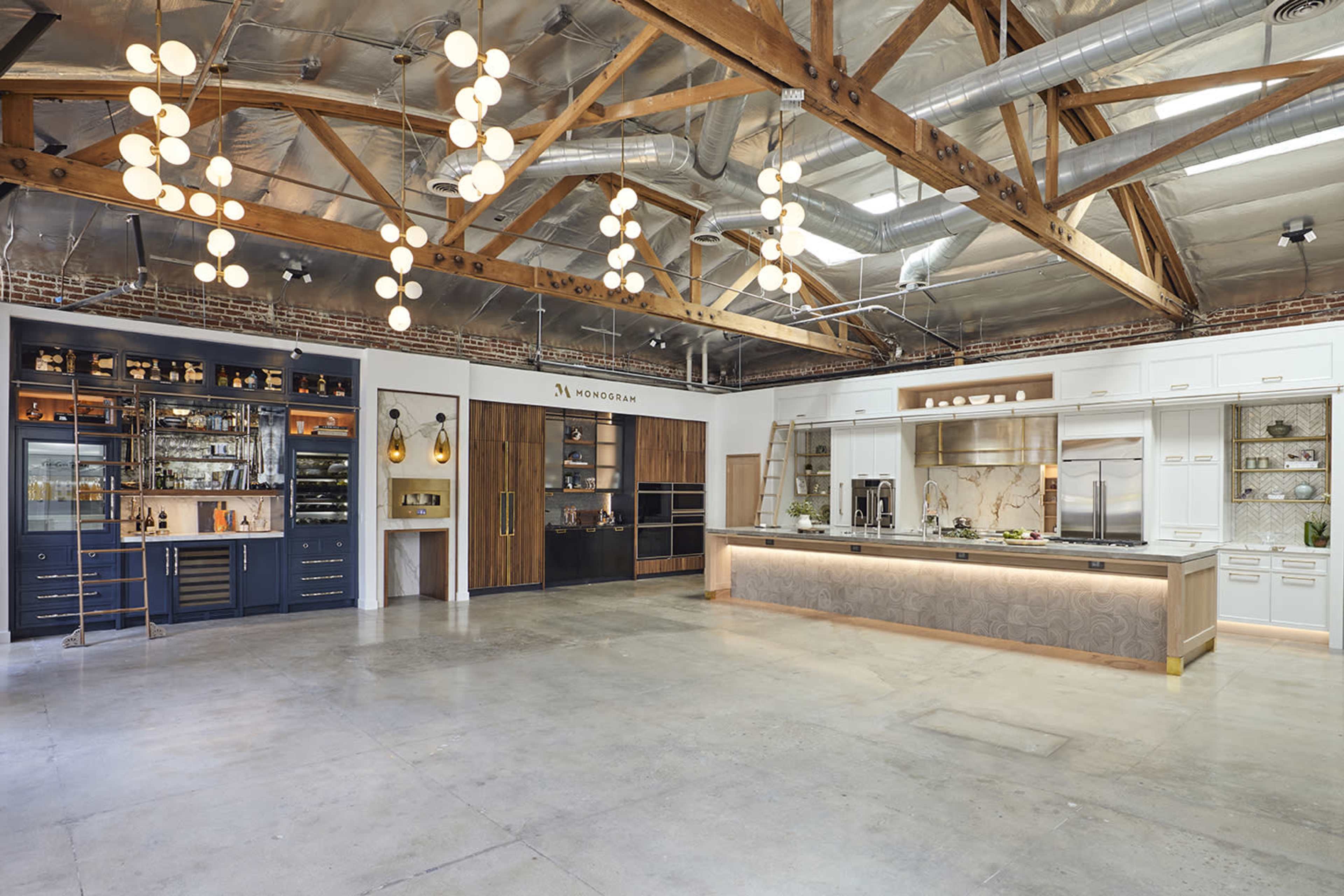 A modern kitchen showroom with wooden beams, pendant lighting, and various cabinetry styles displayed along the walls.