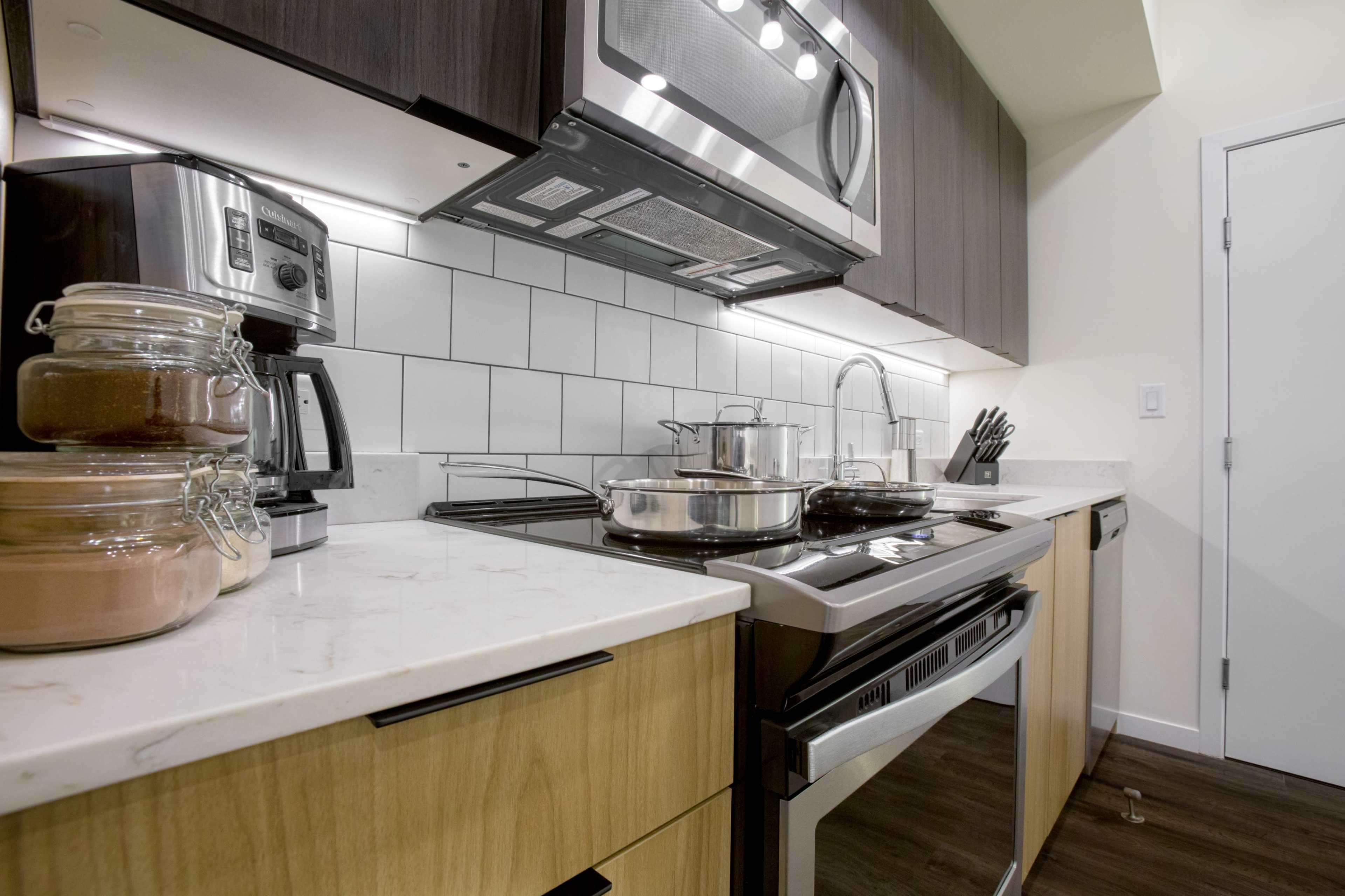 A modern kitchen with a stovetop, microwave, coffee maker, and jars of ingredients on the counter.
