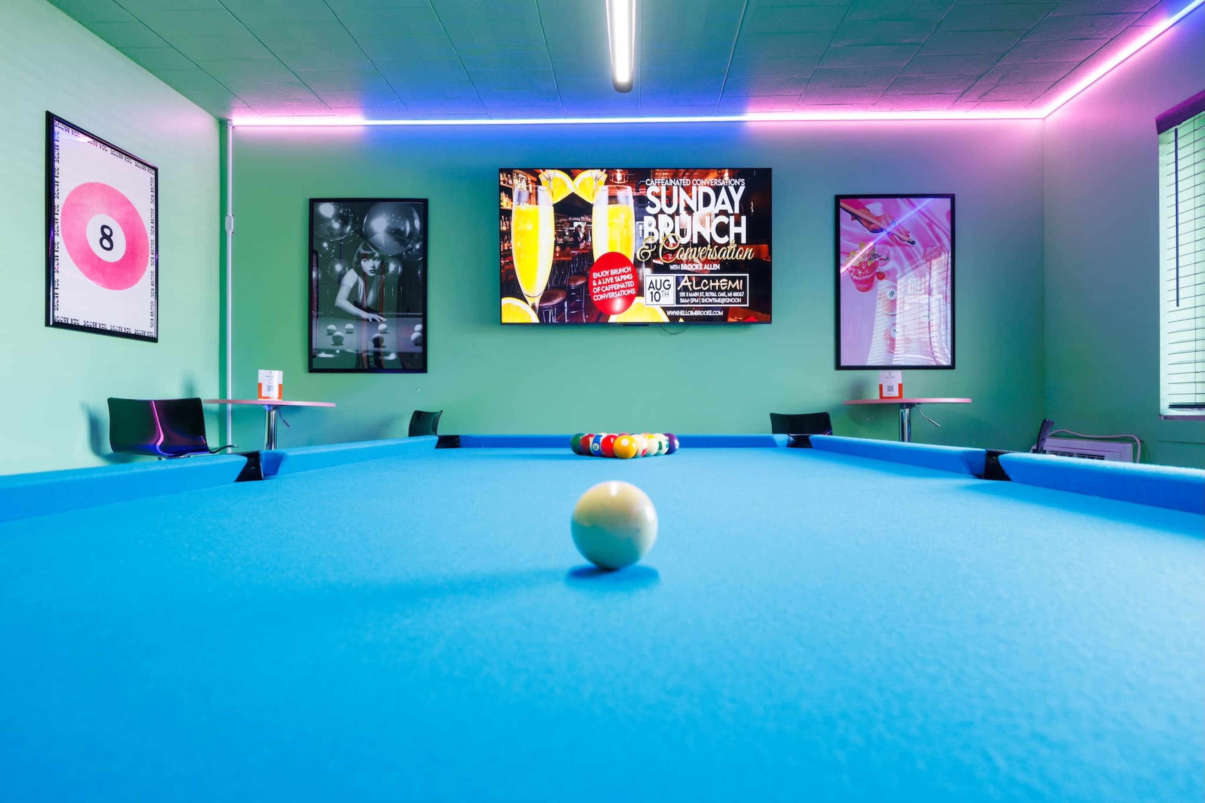 The image shows a vibrant billiard room with a blue pool table in the center, framed by neon lights and colorful posters on the walls.