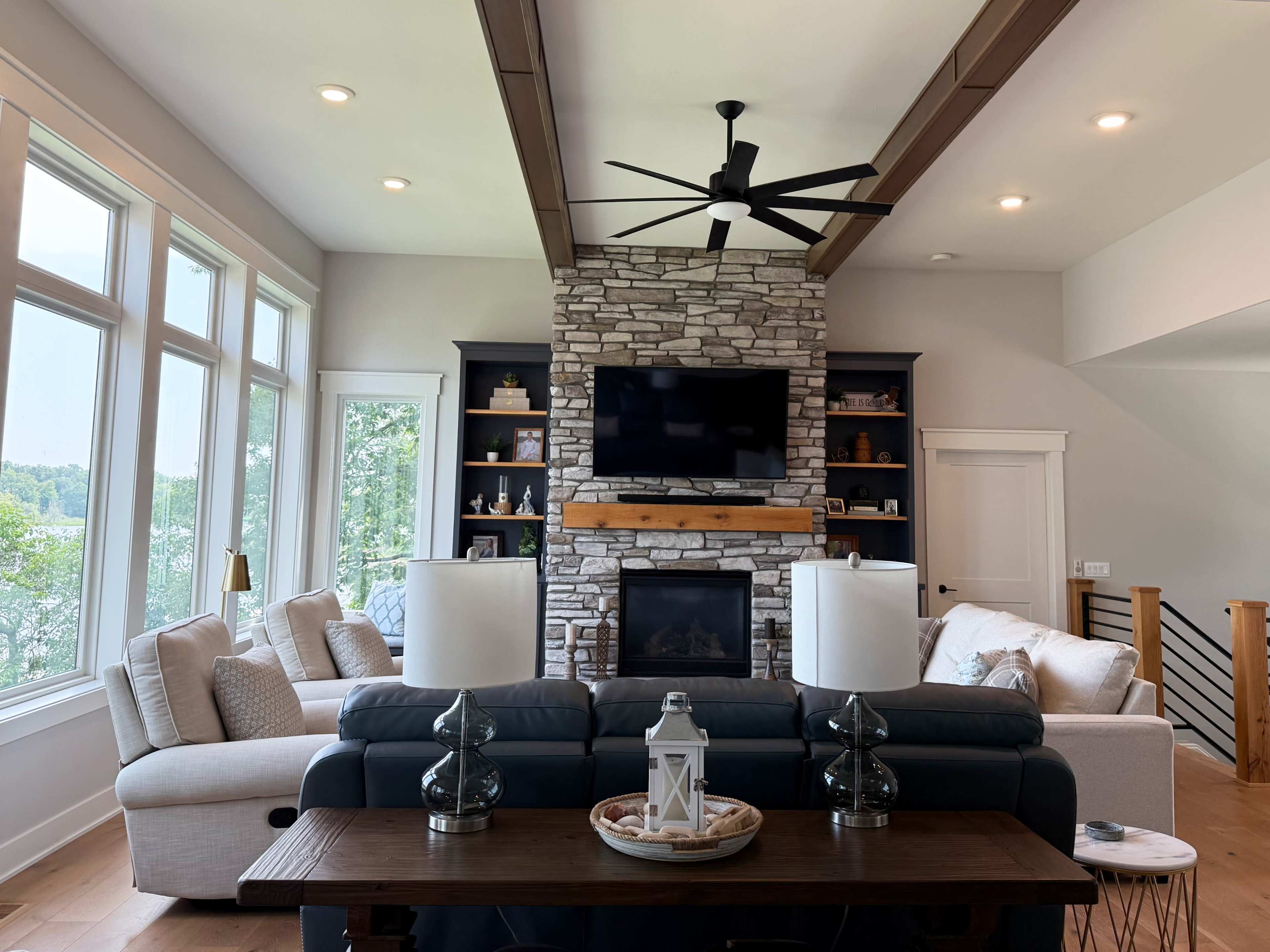 The scene depicts a modern living room featuring a stone fireplace, a large television above it, light-colored furniture, and a coffee table with decorative items.