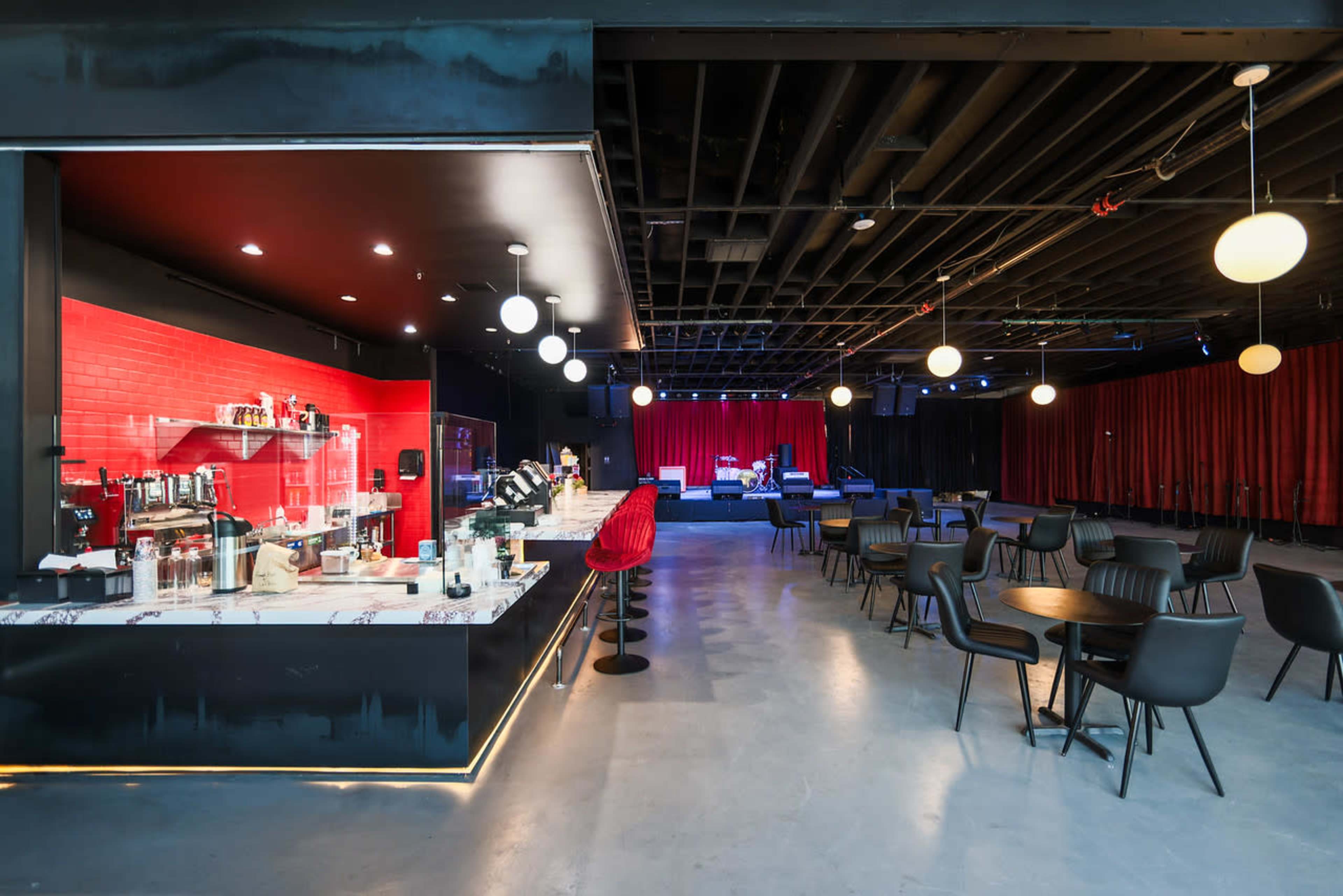 The image shows a modern lounge area with a bar featuring red brick accents, circular pendant lights, and seating arranged for social gatherings.