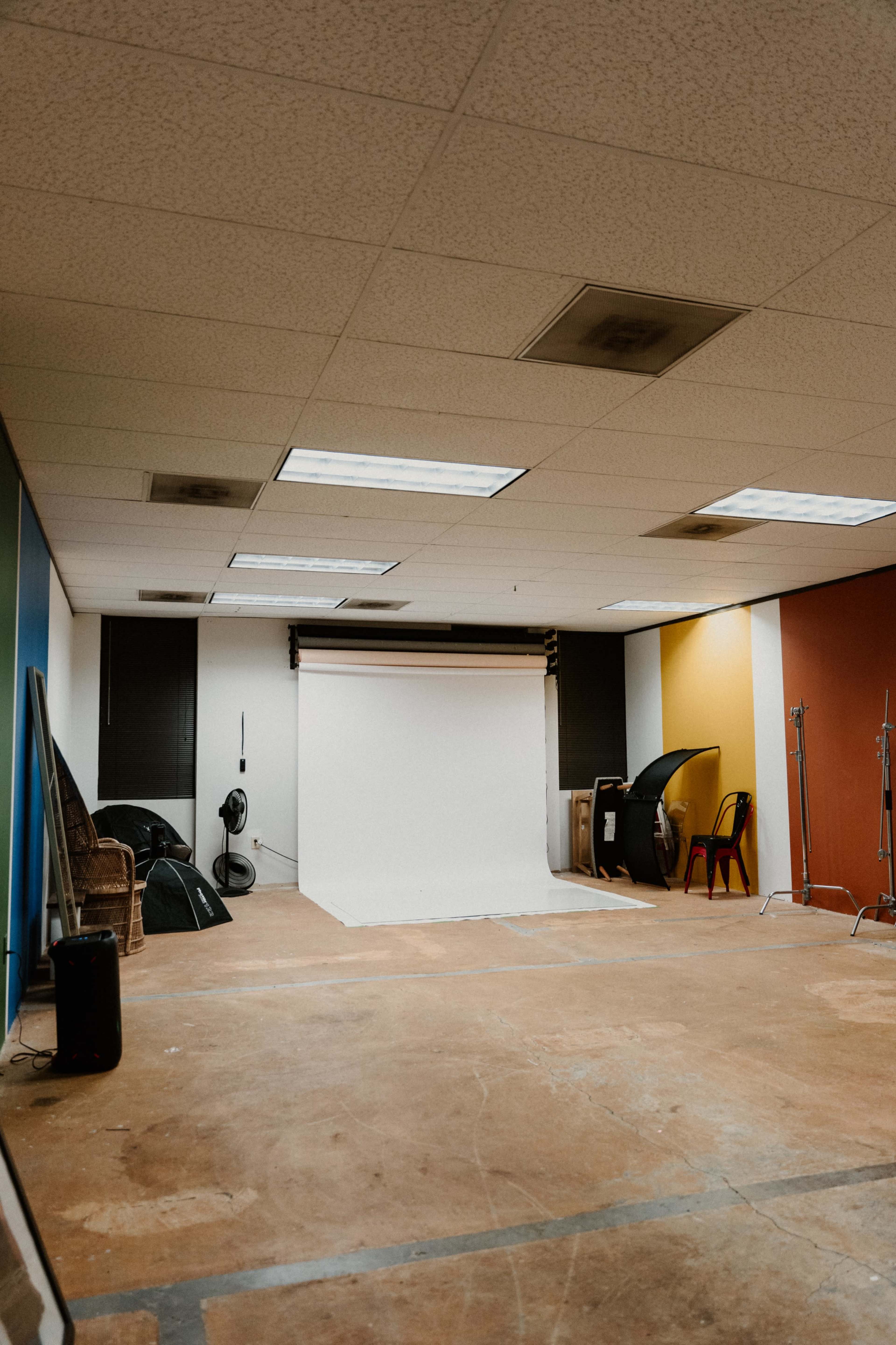 A photography studio with a white backdrop, various lighting equipment, and a mix of colored walls.
