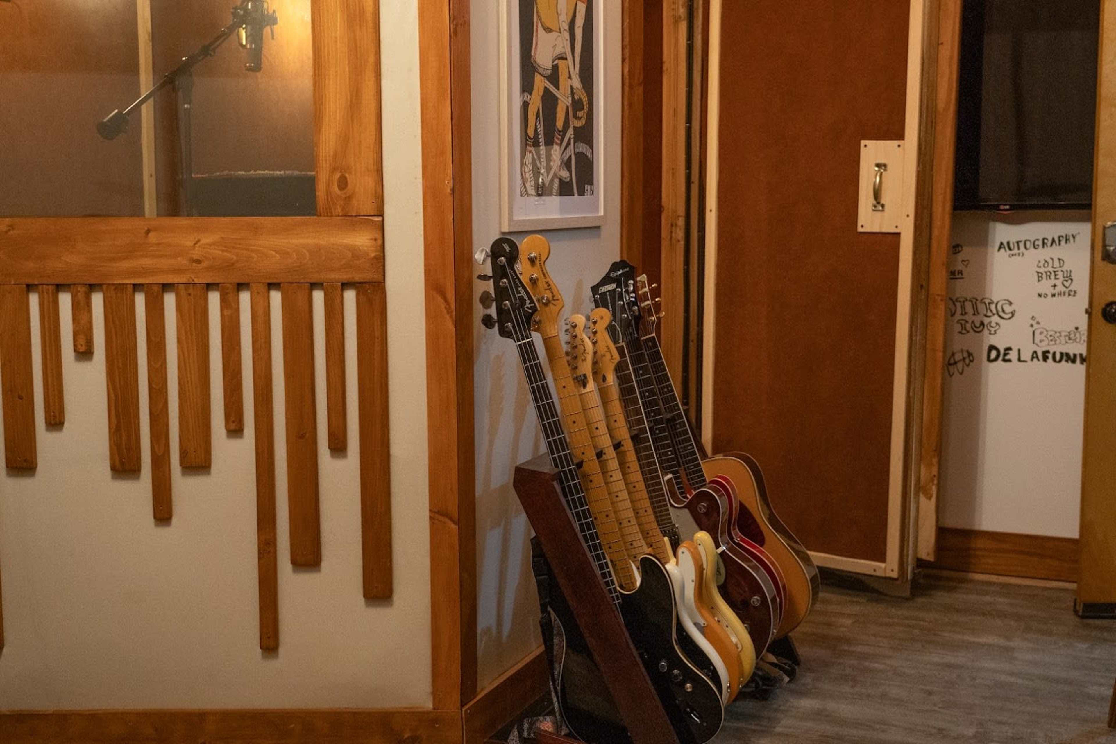 The image shows a music recording studio with a microphone, several guitars propped against a wall, and a partially open door leading to another room.