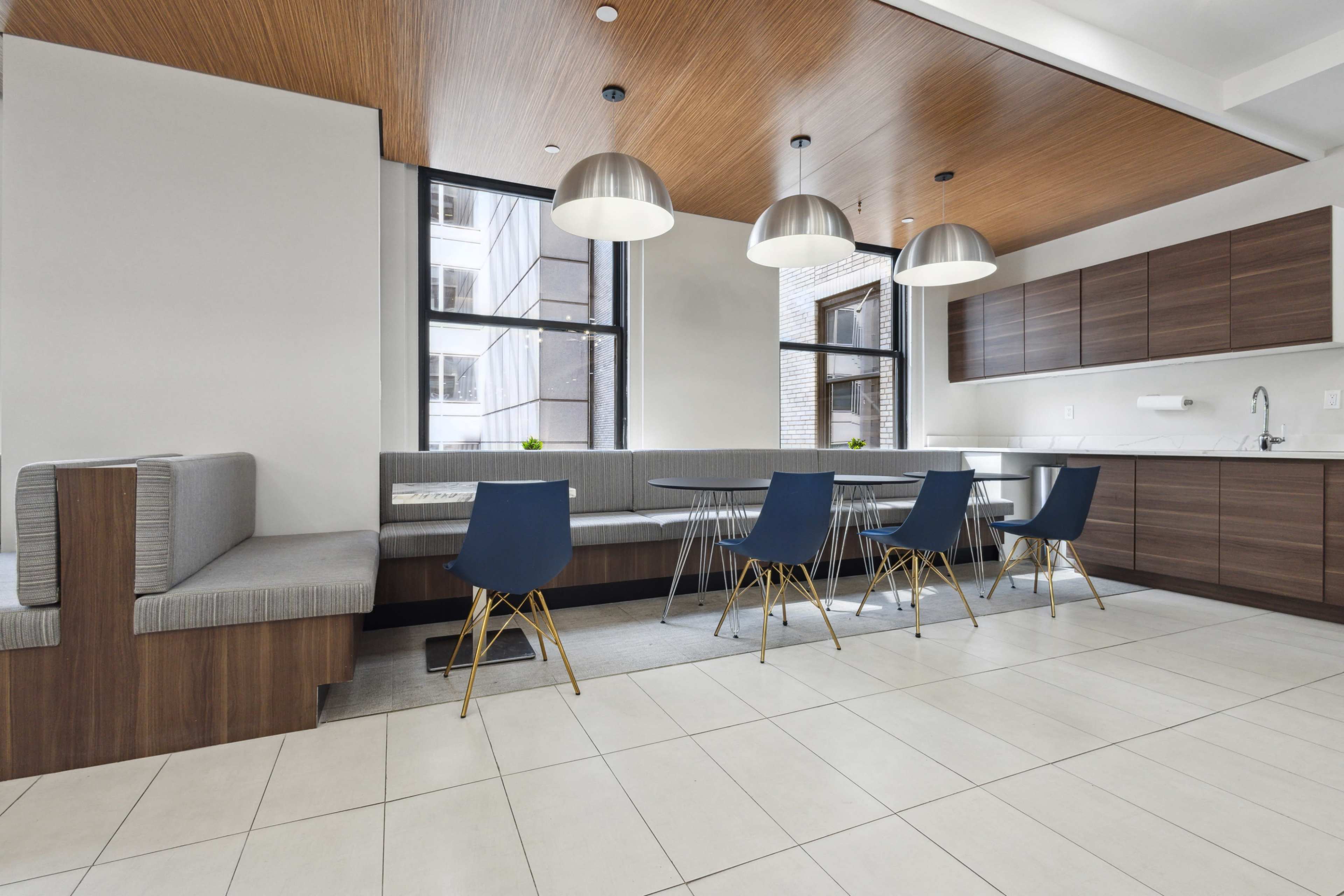 The image shows a modern dining area with a long table surrounded by blue chairs, a built-in bench seating area, and pendant lights above.