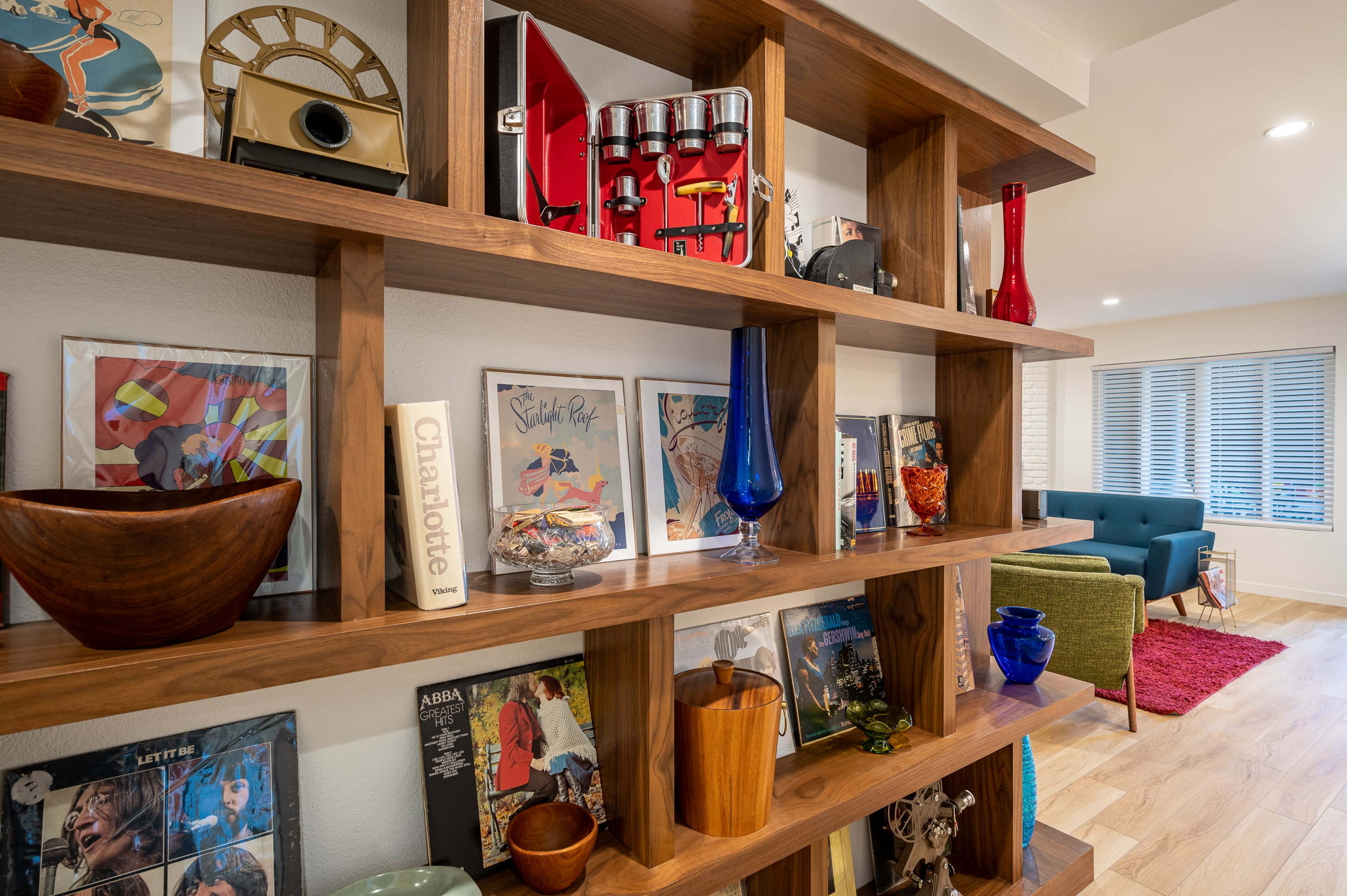 A wooden shelving unit displays various decorative items, vintage records, and framed posters in a modern interior space.
