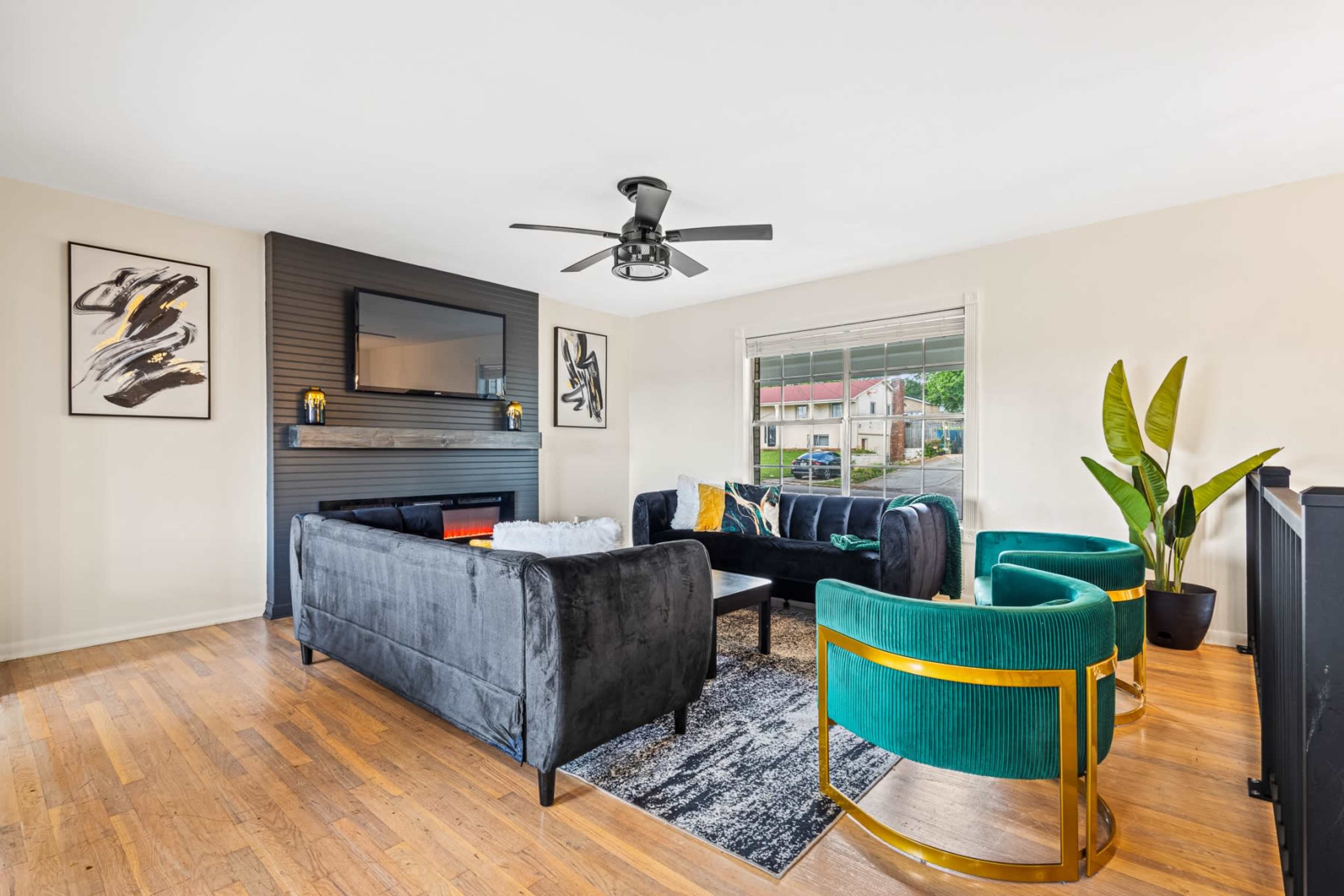 The living room features a black and gray sofa set, green accent chairs, a fireplace, and large windows allowing natural light.