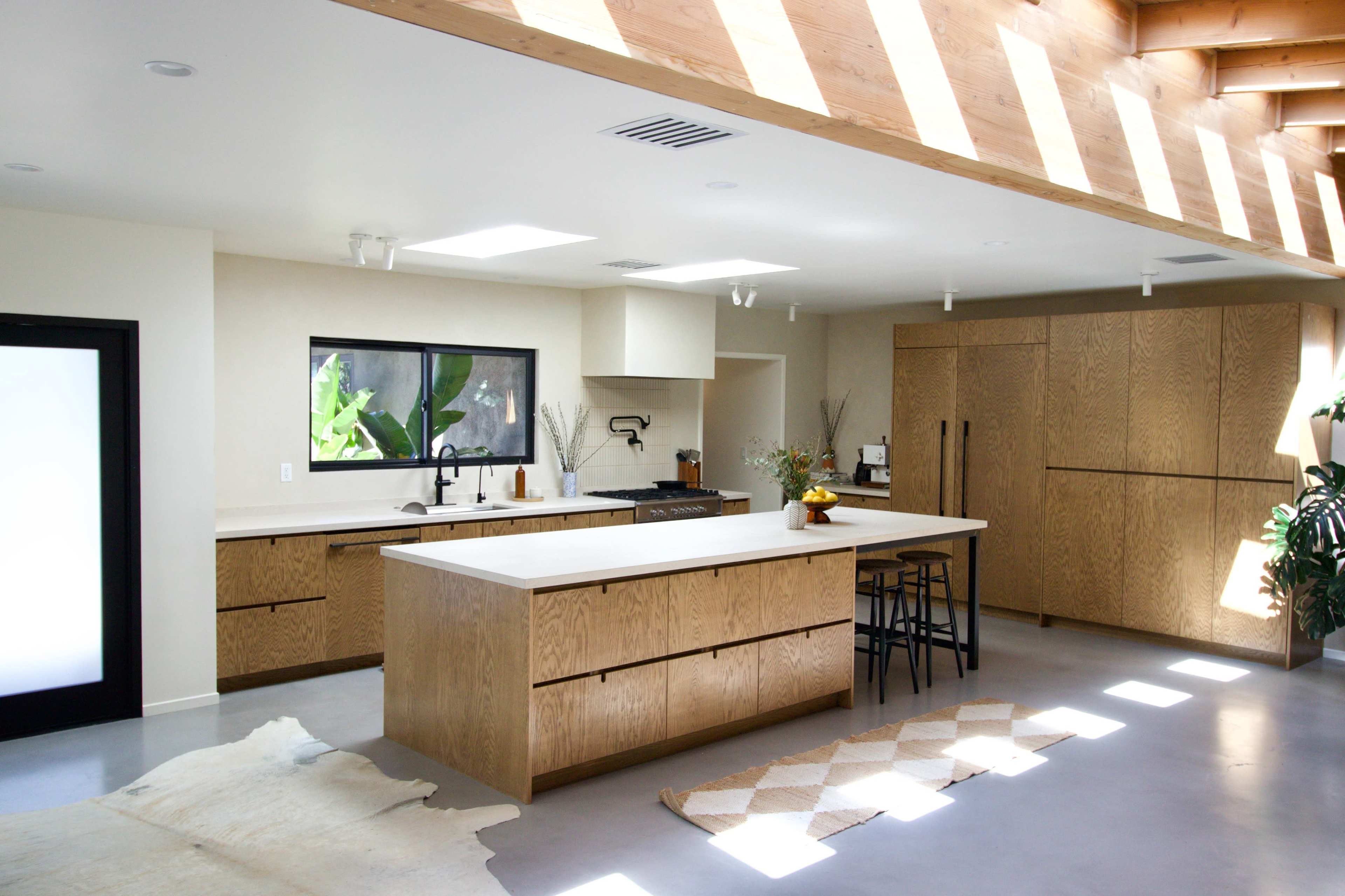 A modern kitchen featuring a large central island, wooden cabinetry, and natural light streaming through skylights.