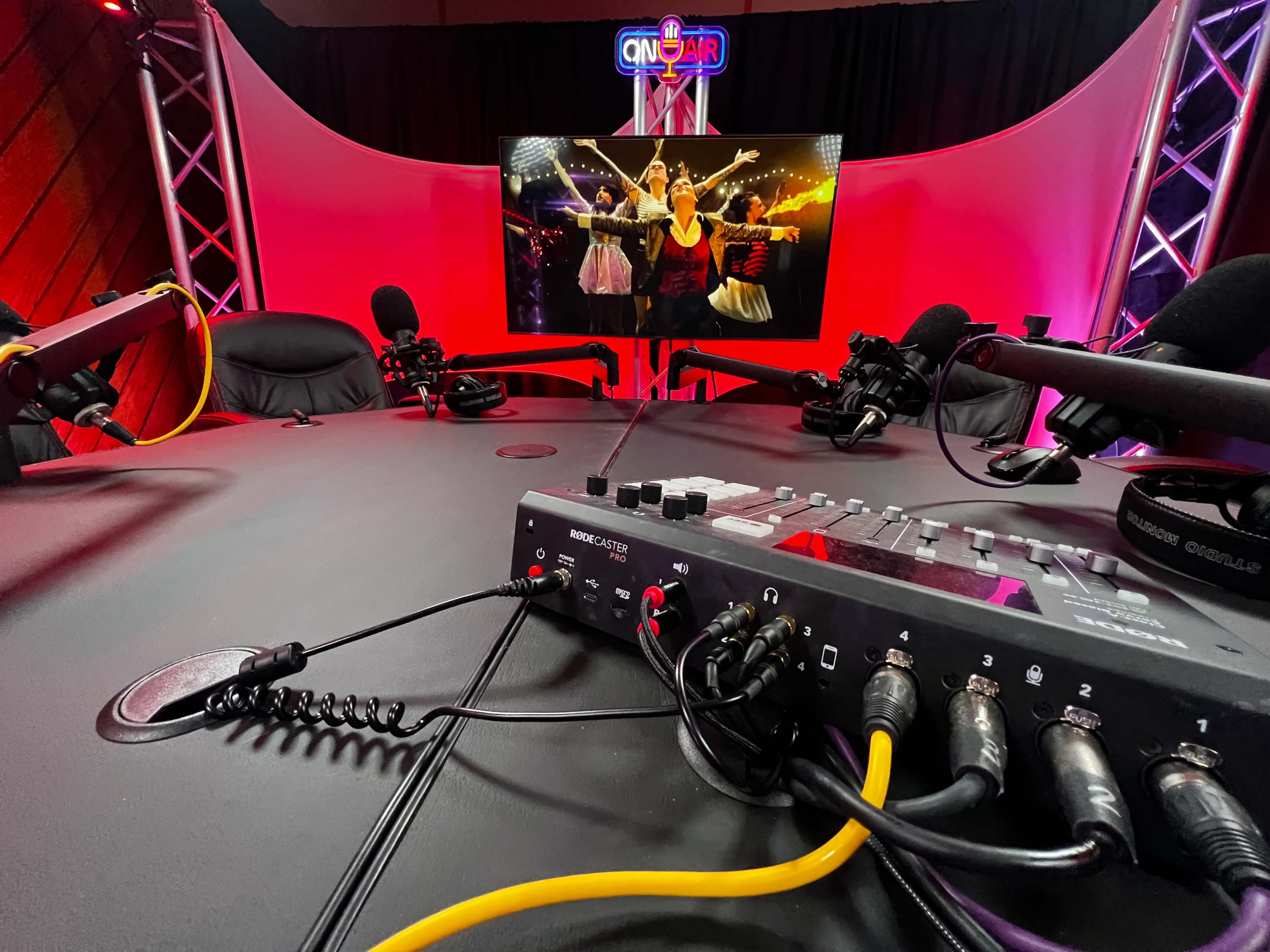 The image shows a broadcast studio with audio equipment in the foreground and a television screen displaying a performance in the background.
