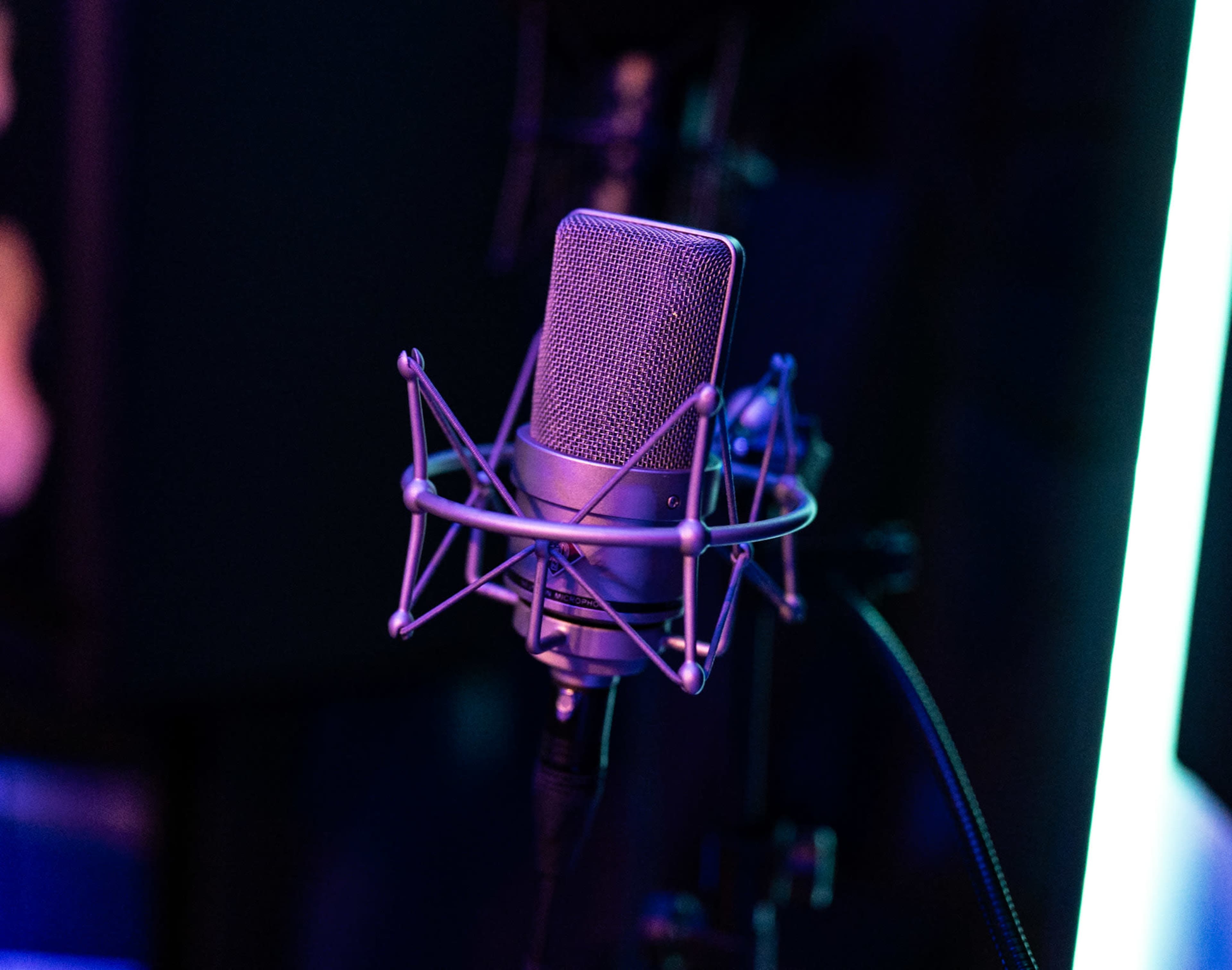 A microphone is mounted in a shock mount, set against a dark background with colorful lighting.