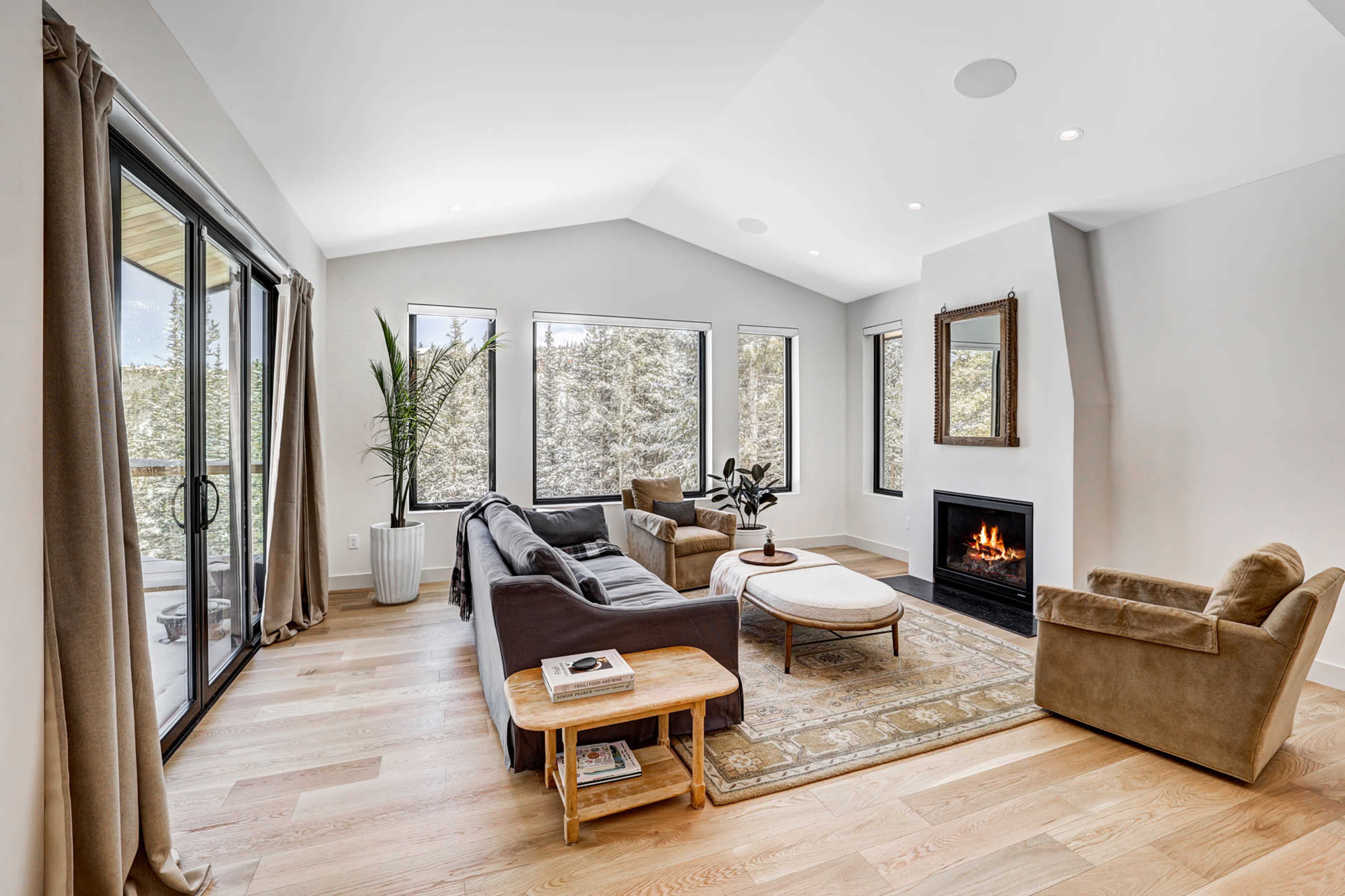 A modern living room with large windows, a fireplace, and a combination of seating areas including a sofa, a chair, and a coffee table.