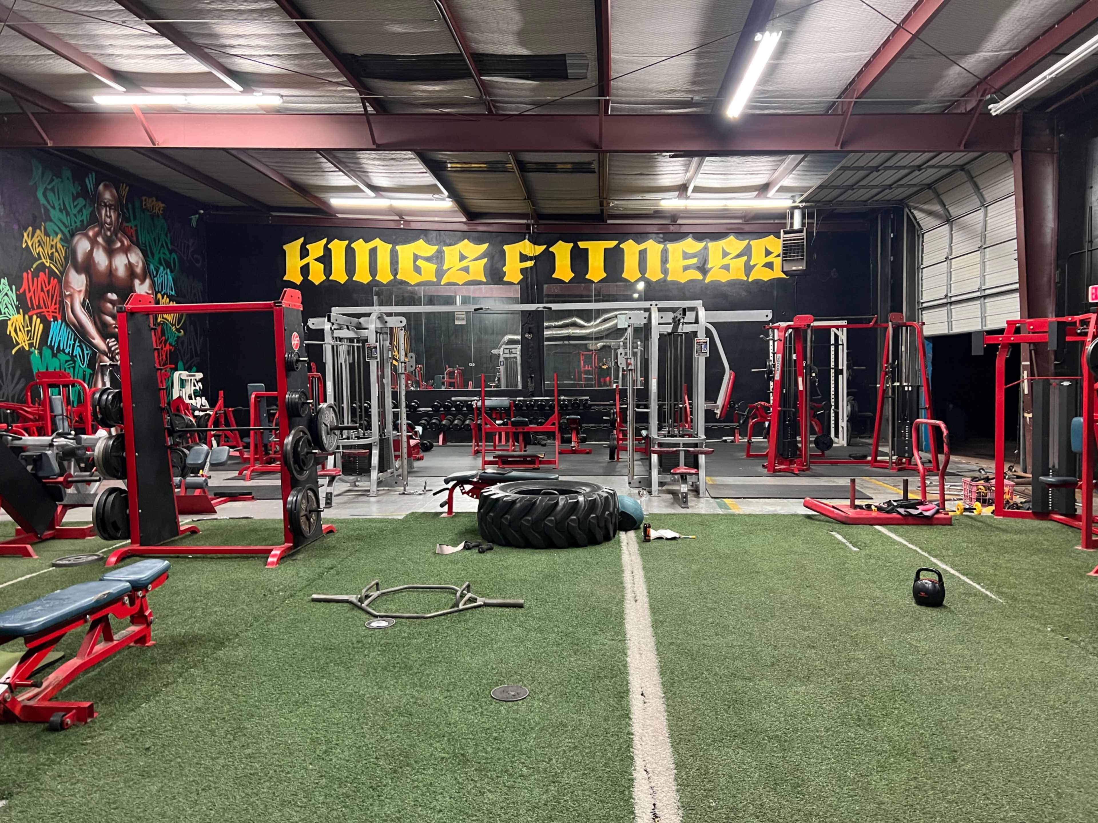 The image shows a gym called "Kings Fitness" featuring various workout equipment, including weightlifting machines and free weights, set against a vibrant mural backdrop.