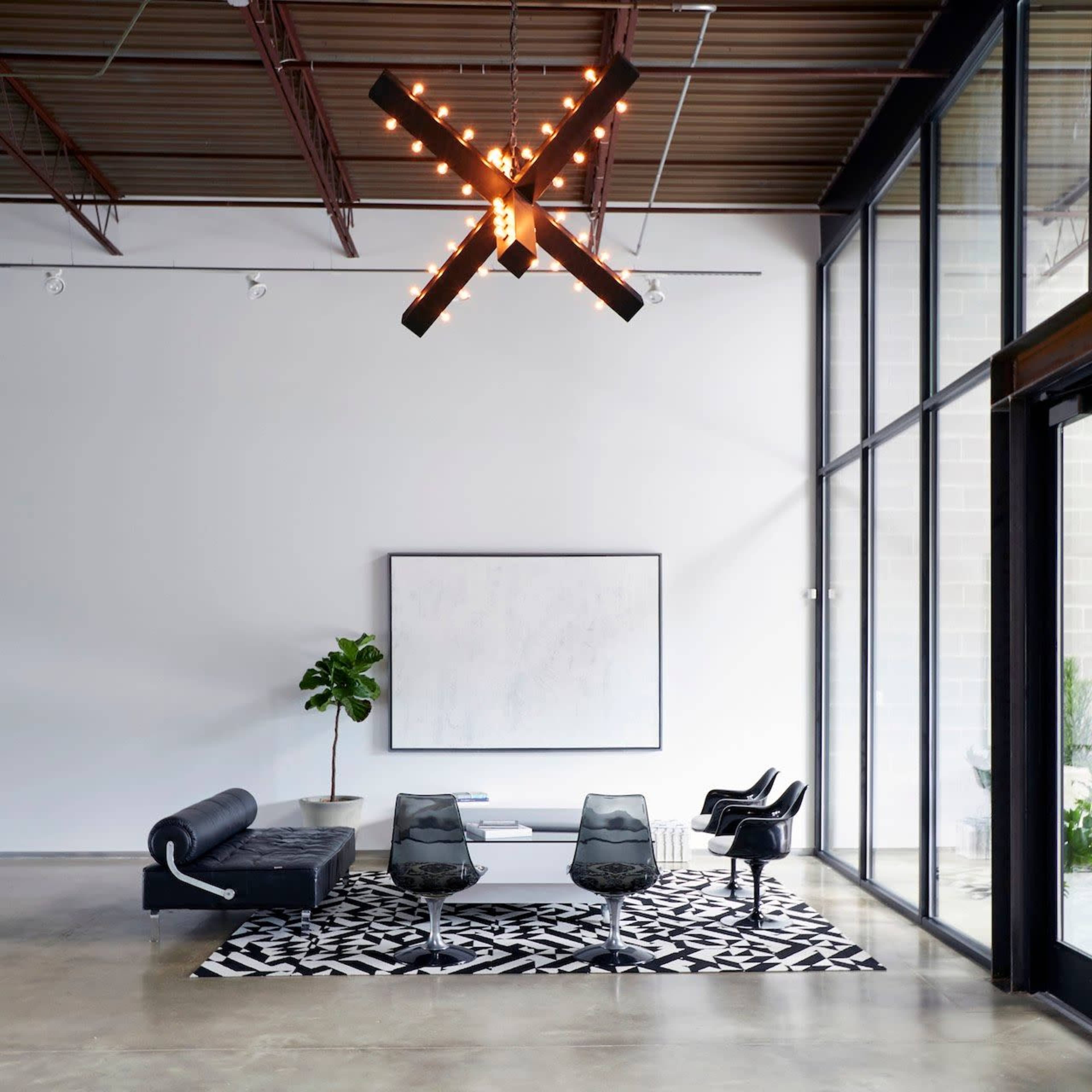 A modern interior space featuring a black leather sofa, two sleek chairs, a geometric rug, and a large pendant light suspended from the ceiling.
