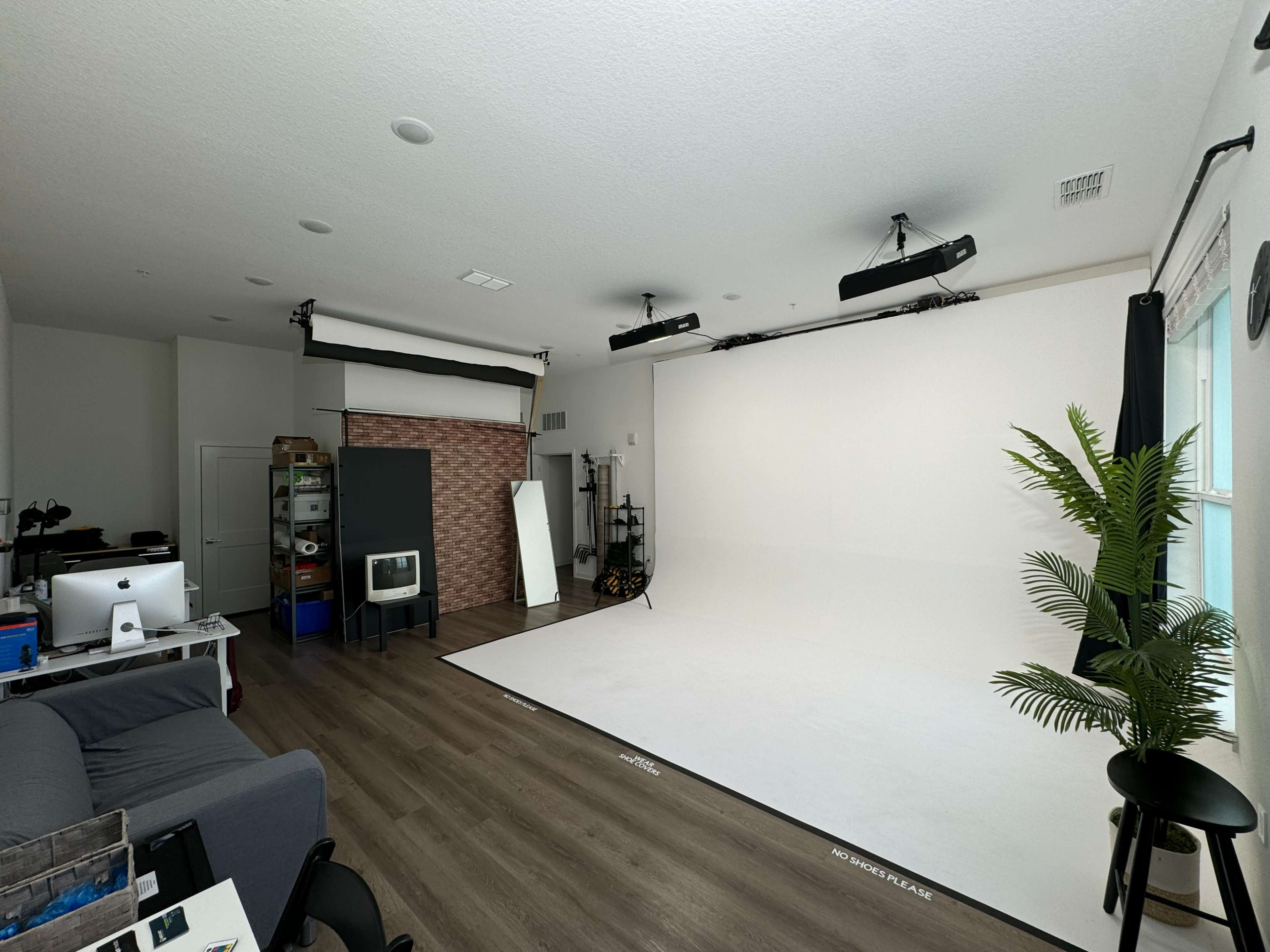 The image shows a spacious photography studio with a large white backdrop, soft lighting, and various props and equipment arranged around the room.