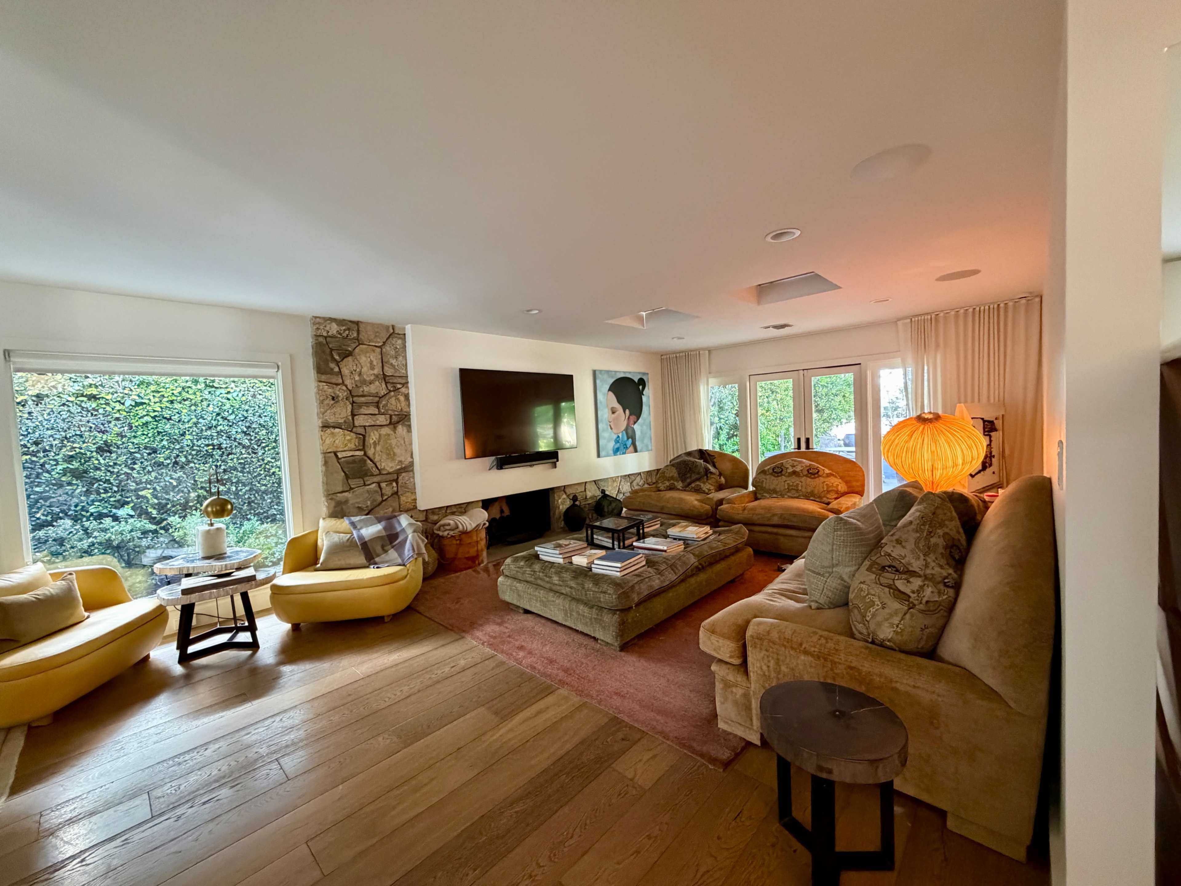 The living room features a light-filled space with stone accents, multiple seating arrangements, and large windows overlooking greenery.