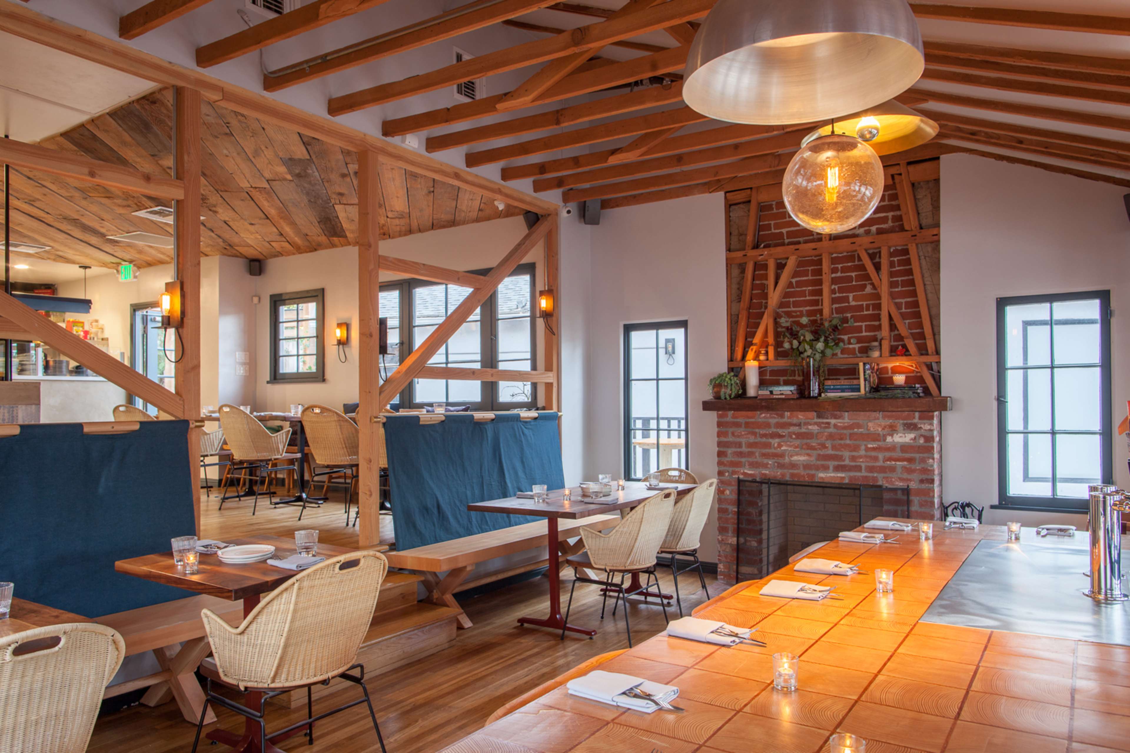 The image shows a restaurant interior featuring wooden beams, a brick fireplace, and tables set for dining.