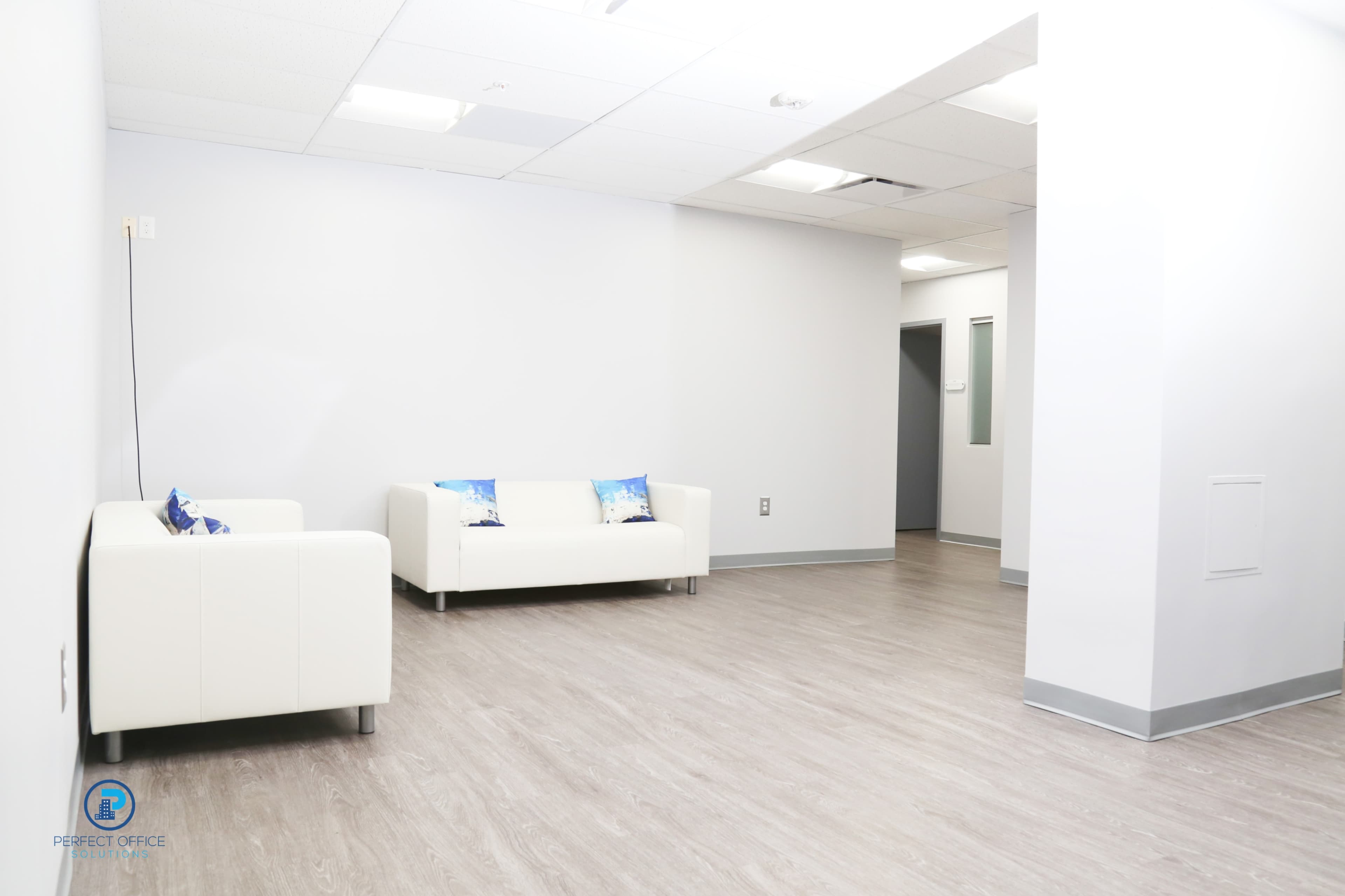 A minimalist office space with two white sofas and light-colored flooring.