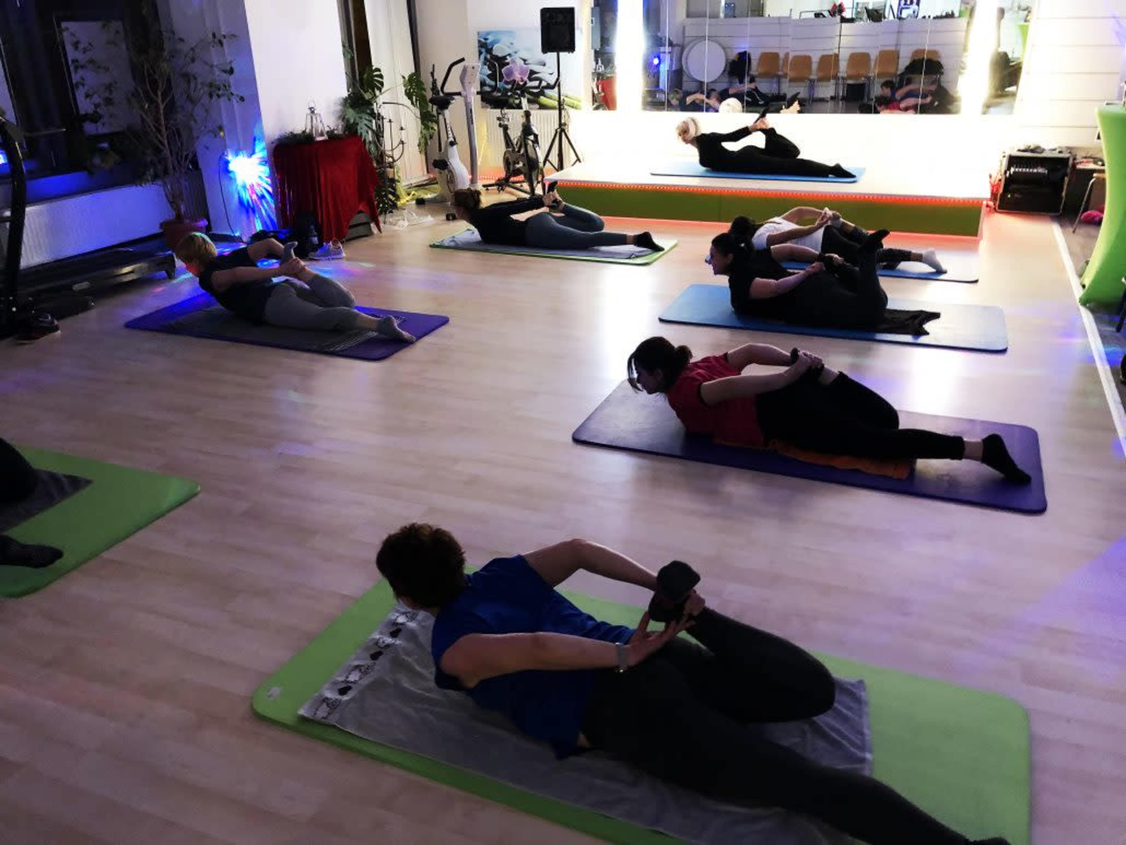 A group of people are practicing yoga on mats in a well-lit studio.