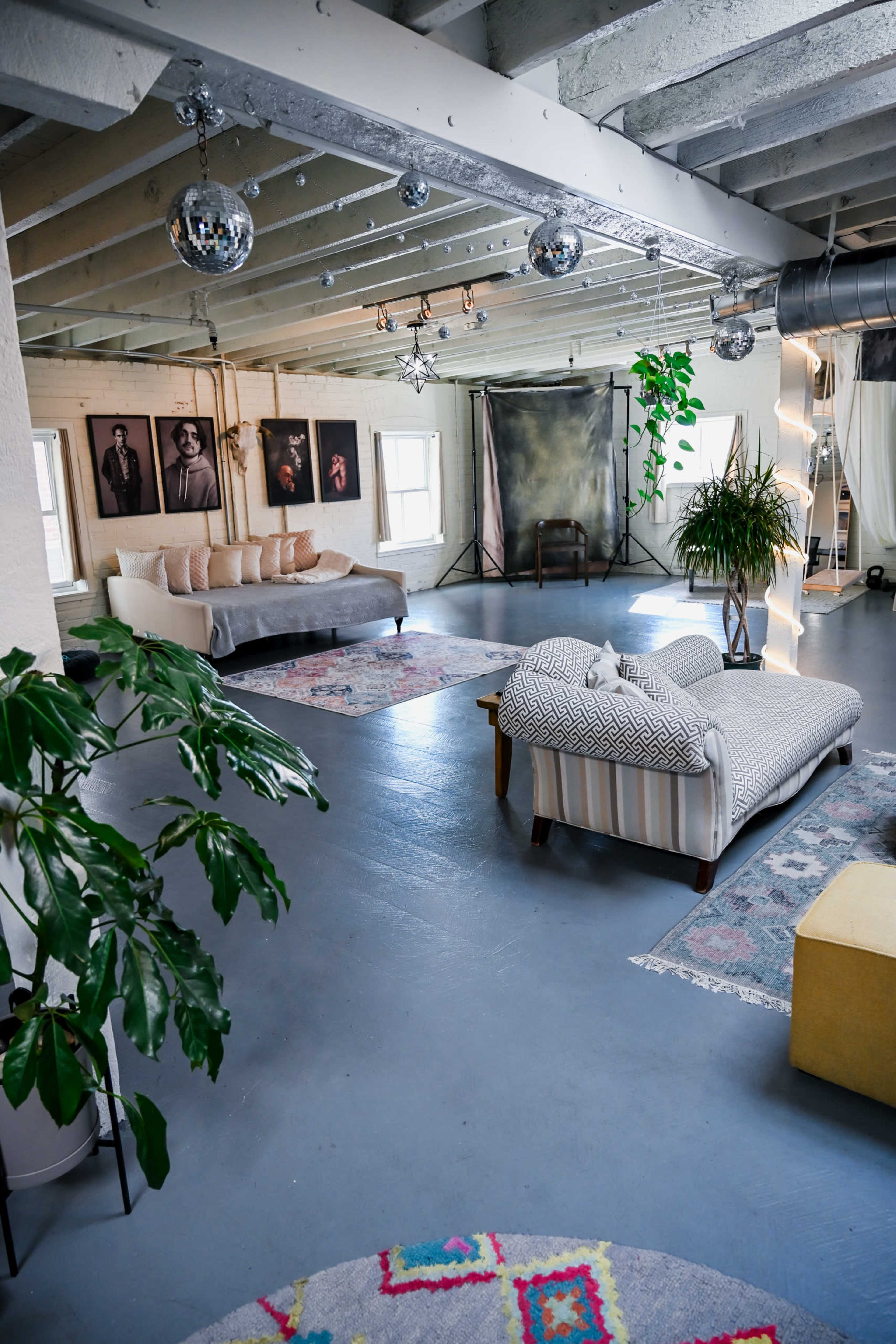 The image shows a spacious, well-lit interior with various seating options, large plants, and framed photographs on the walls.