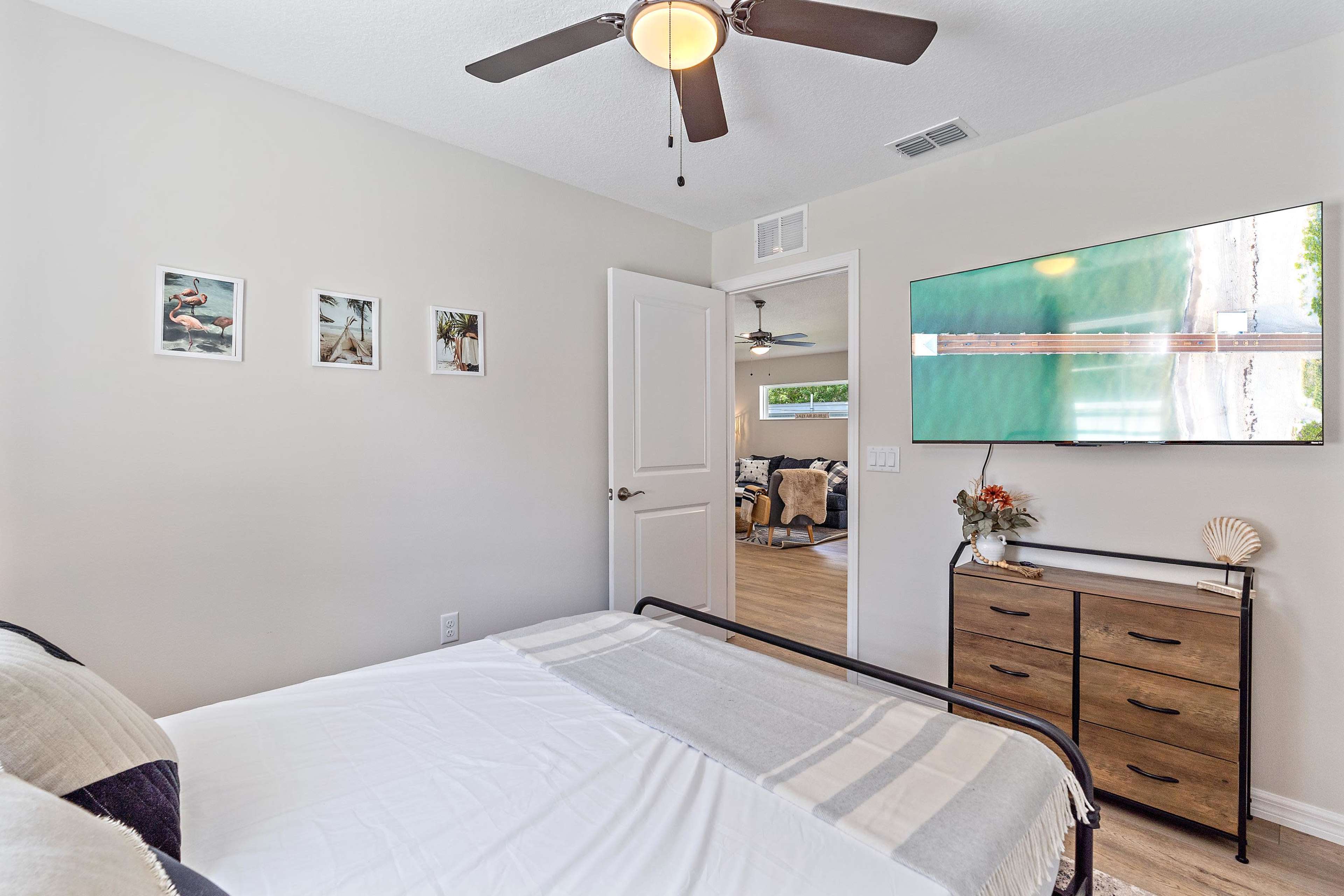 A bedroom with a bed, a ceiling fan, a television mounted on the wall, and framed pictures hanging near the door.