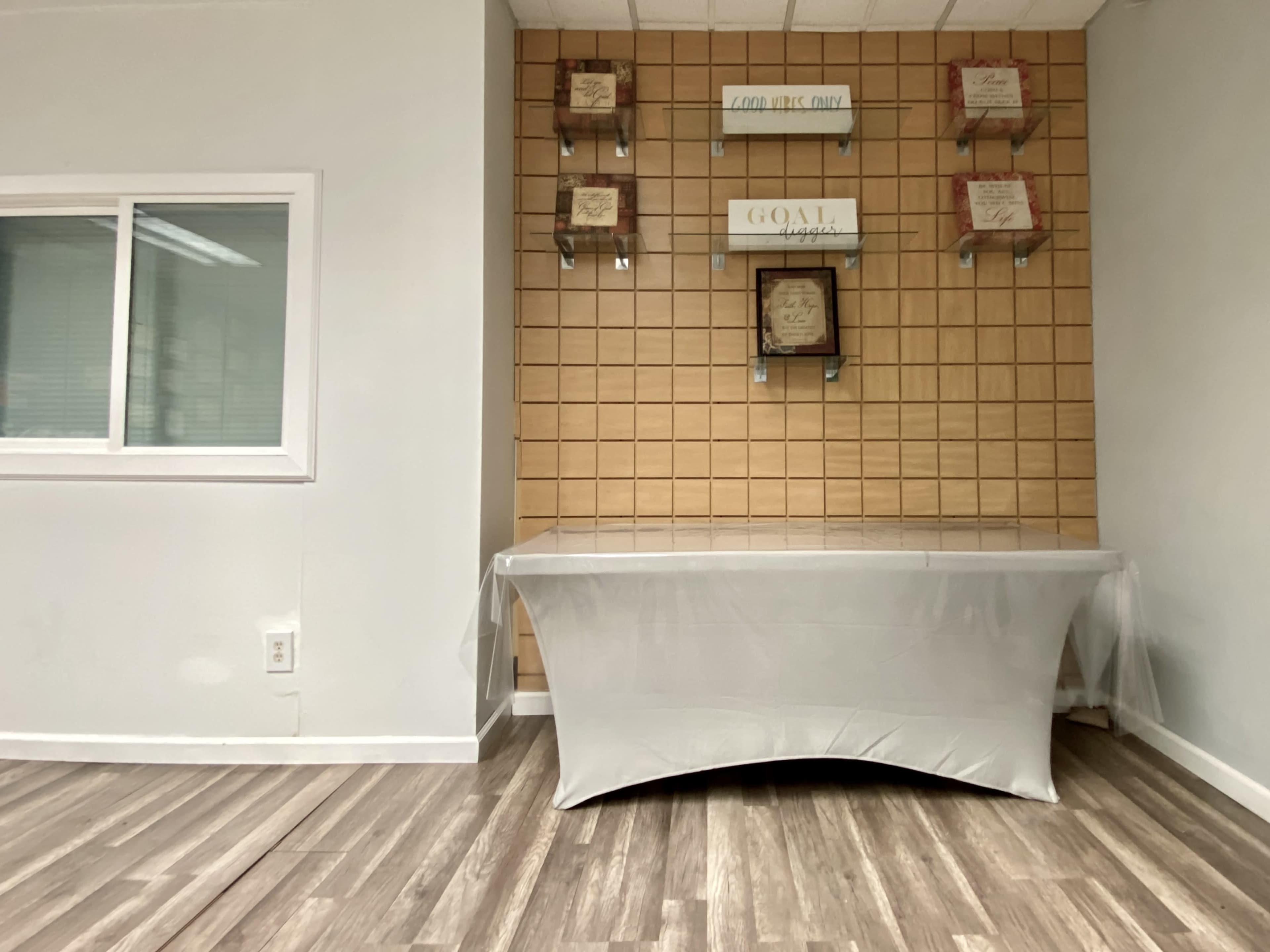 A table draped with a white cover is set against a wooden-paneled wall featuring decorative shelves and framed signs.