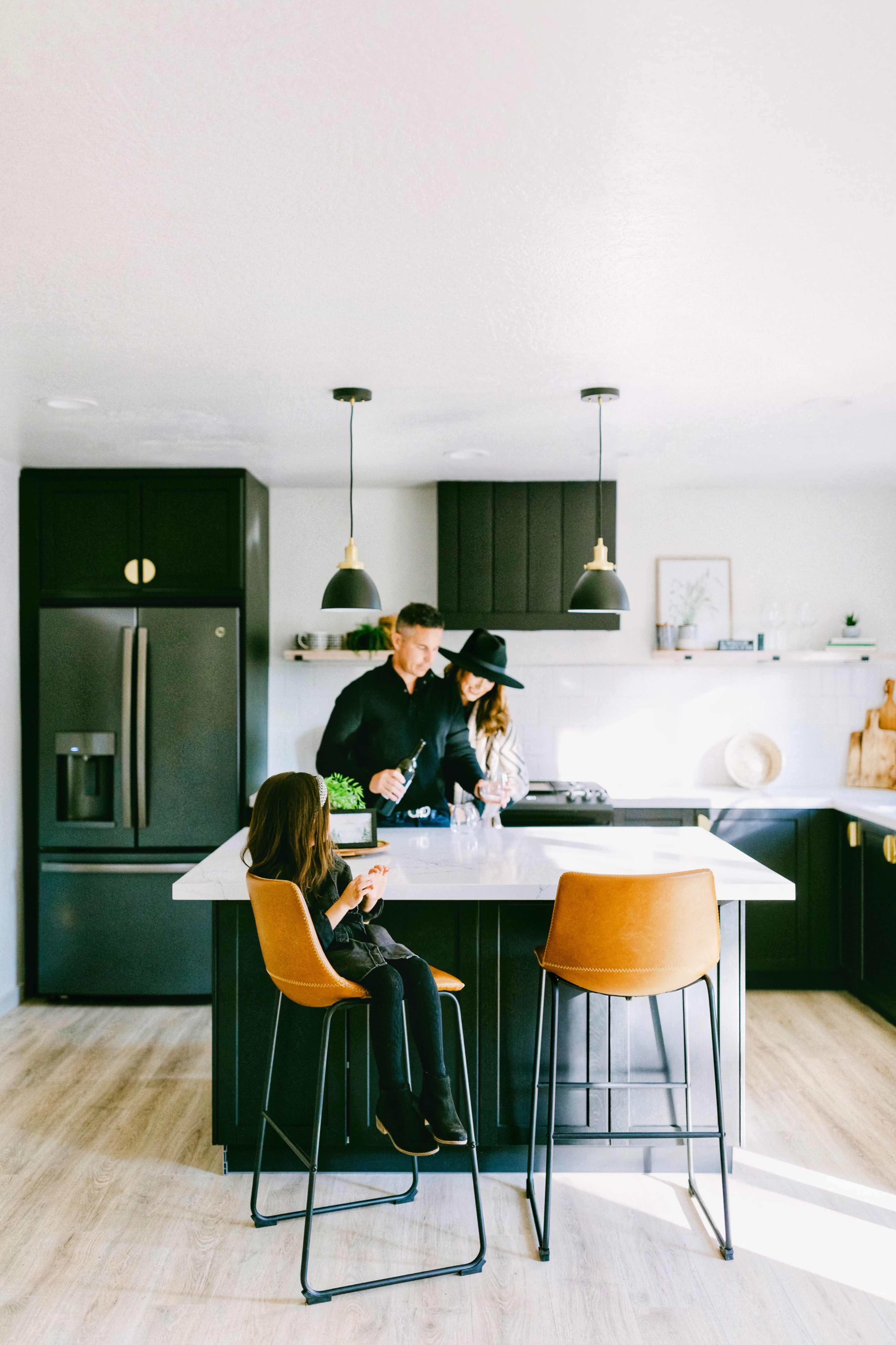 A family of three is preparing food in a modern kitchen with black cabinetry and a marble island.