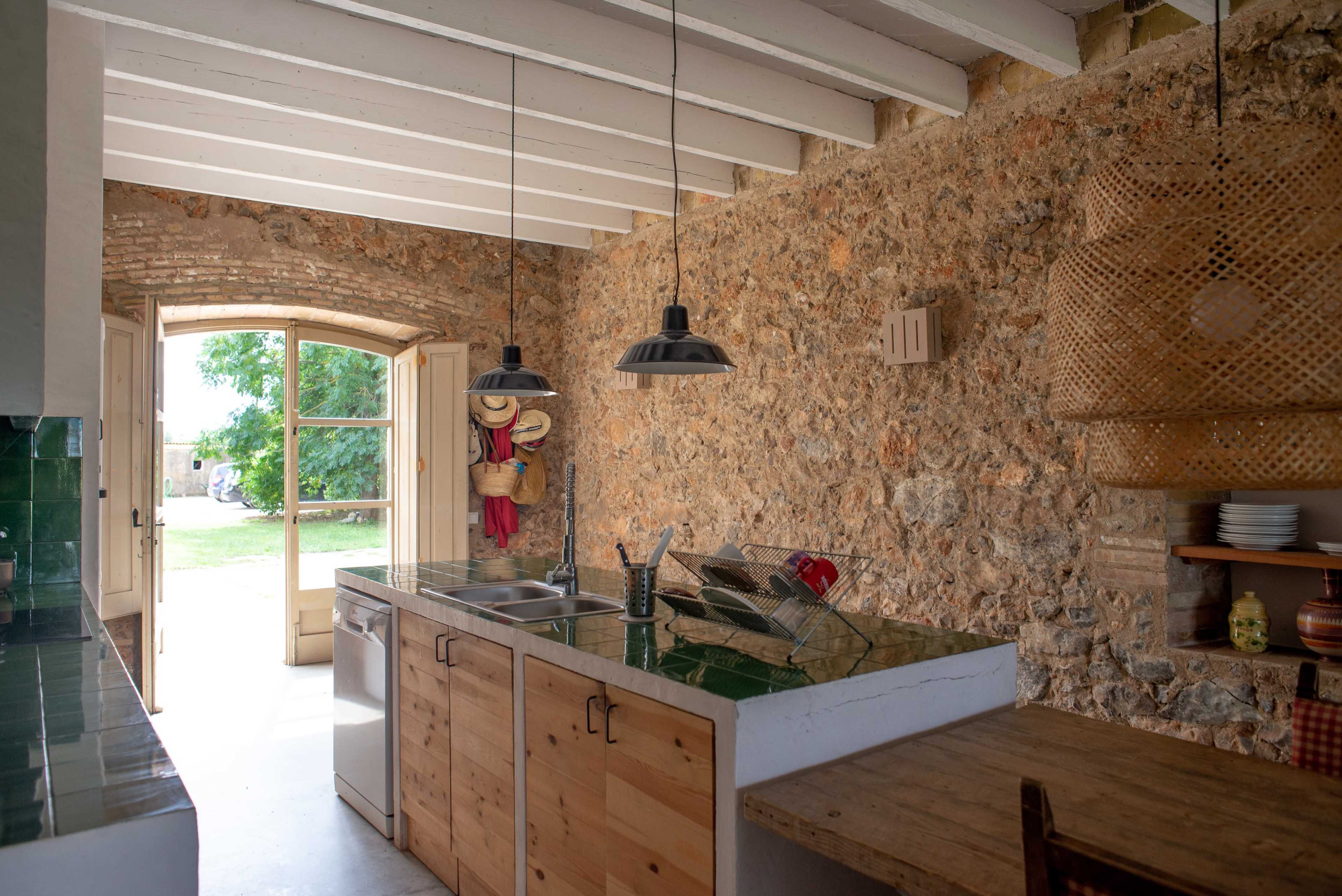 The kitchen features exposed stone walls, wooden cabinetry, and a view of a garden through an arched door.